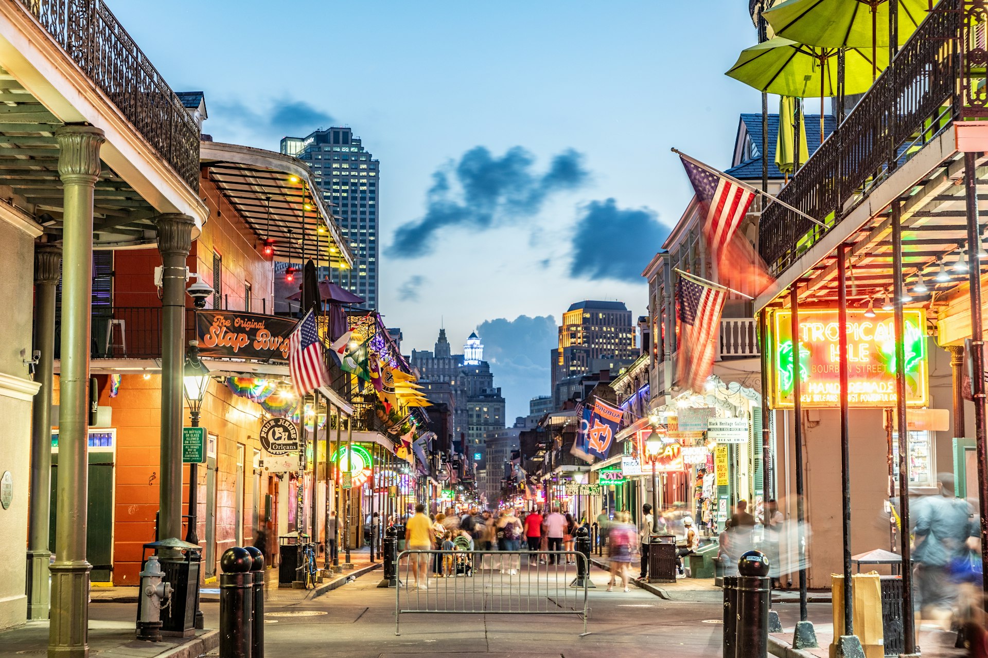 People walk along a neon-lit city street as evening falls