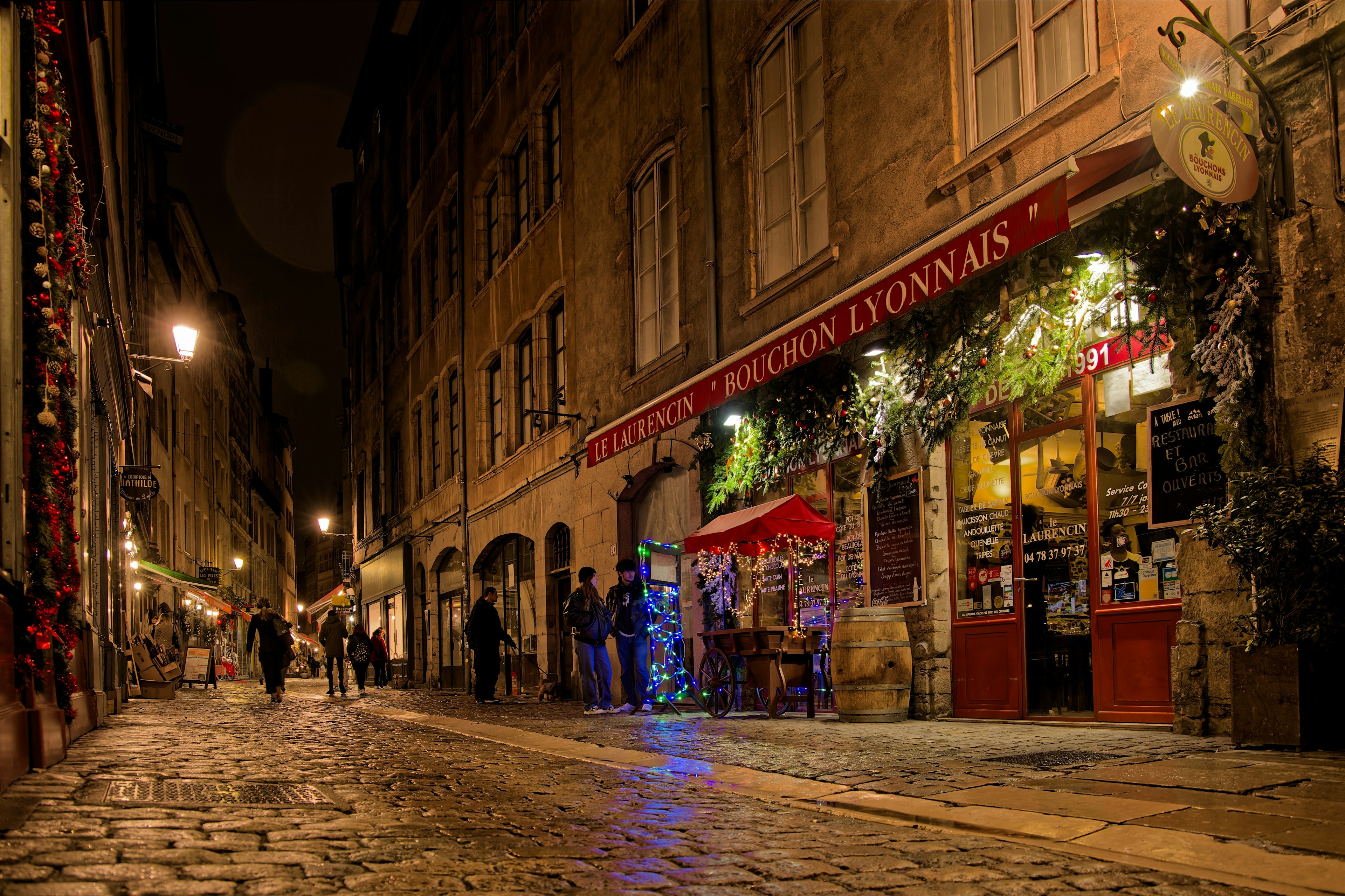 A cobbled street lined with restaurants is lit up at night
