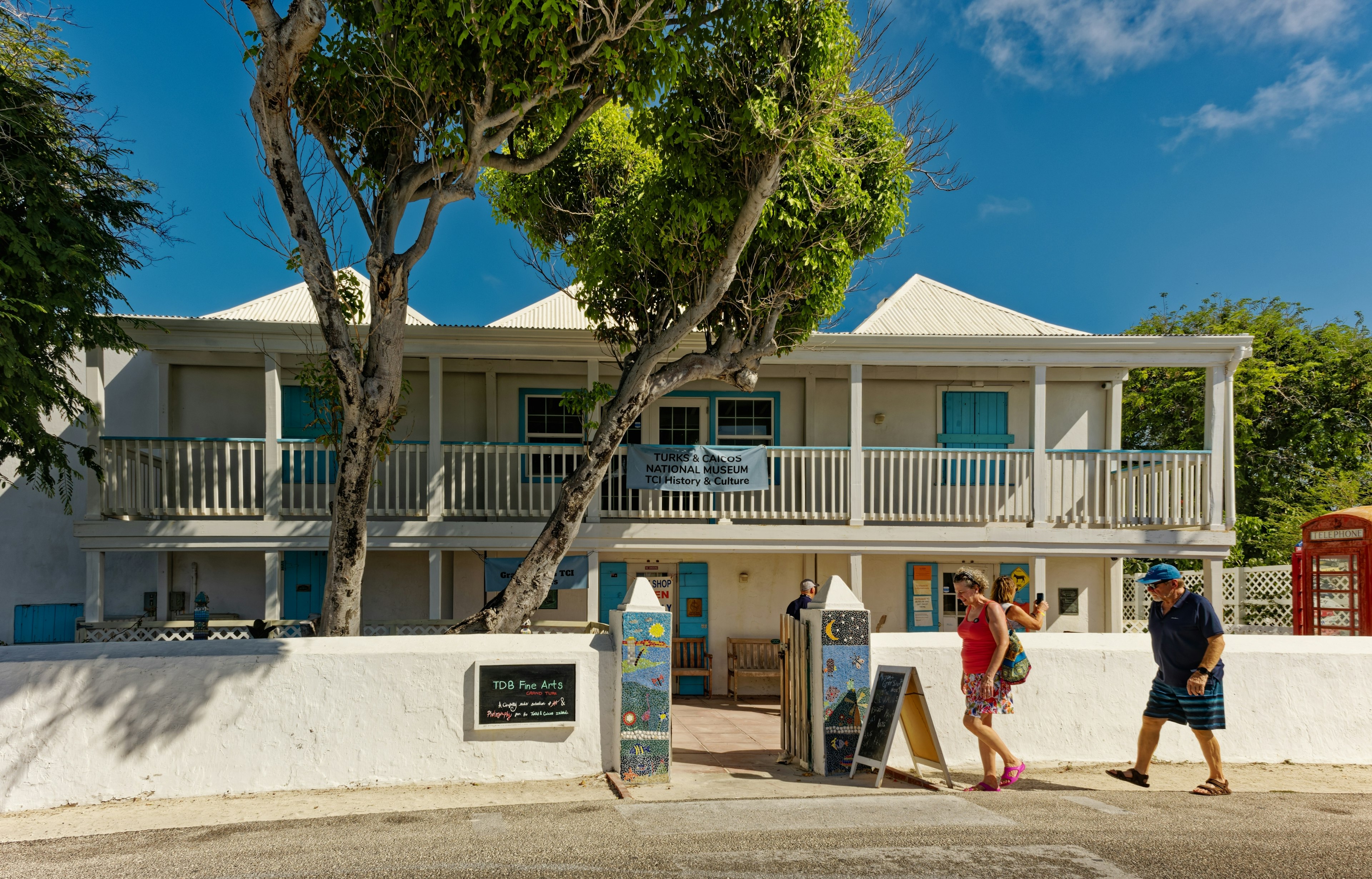 Tourists walk past the modest whitewashed building that houses the Turks and Caicos National Museum on a bright sunny day. | Learn about the islands' heritage at the Turks and Caicos National Museum on Grand Turk. Darryl Brooks/Shutterstock