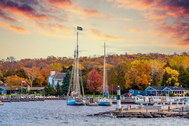 A small harbor town with sail boats moored in the dock. Trees are all golden marking autumn months