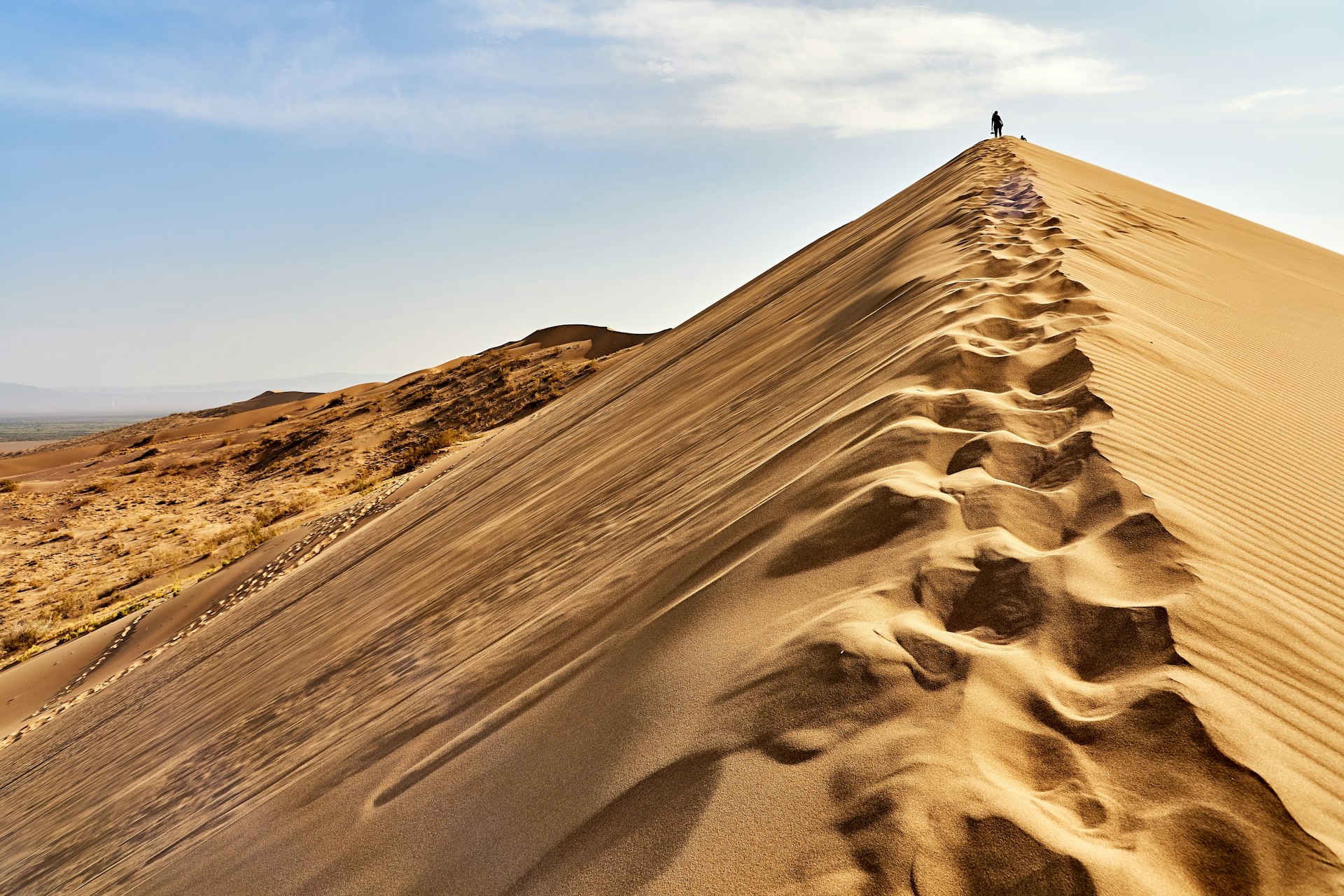 A sole figure in silhouette walks along the peak of a sand dune