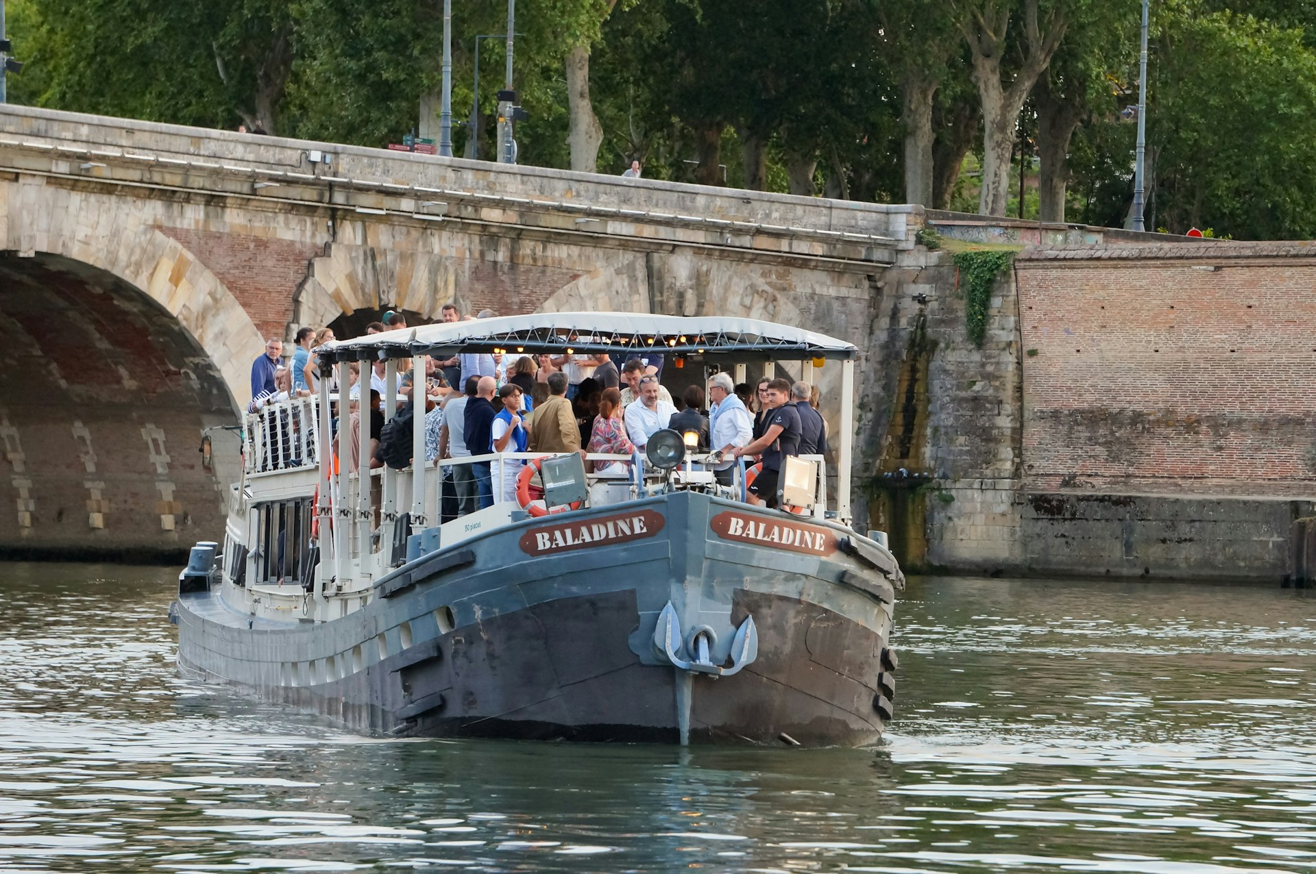 Baladine cruise barge sailing on the Garonne River by Pont-Neuf Bridge and Daurade Port in the evening, Toulouse