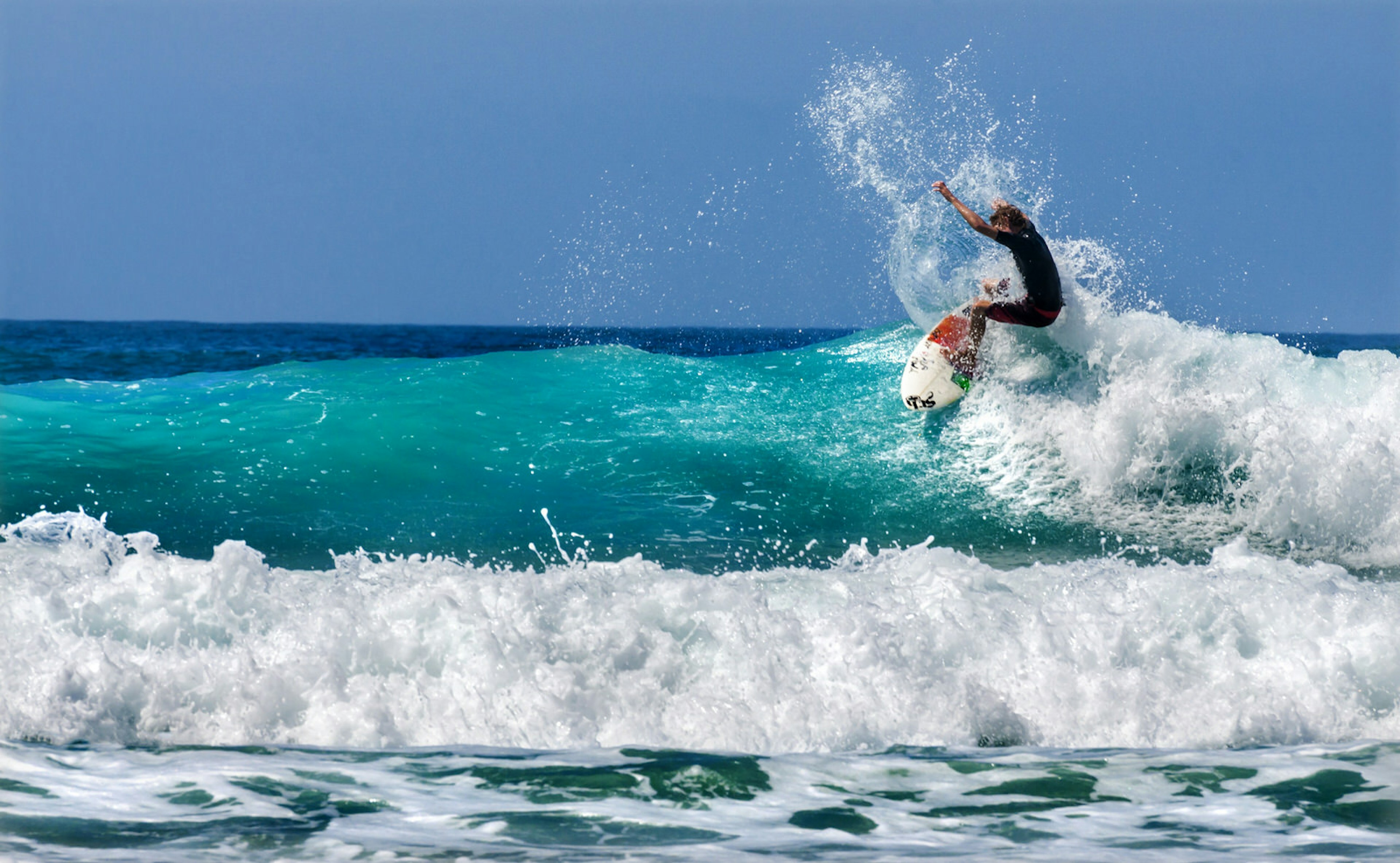 A surfer catches a turquoise wave - backdropped by bright blue sky