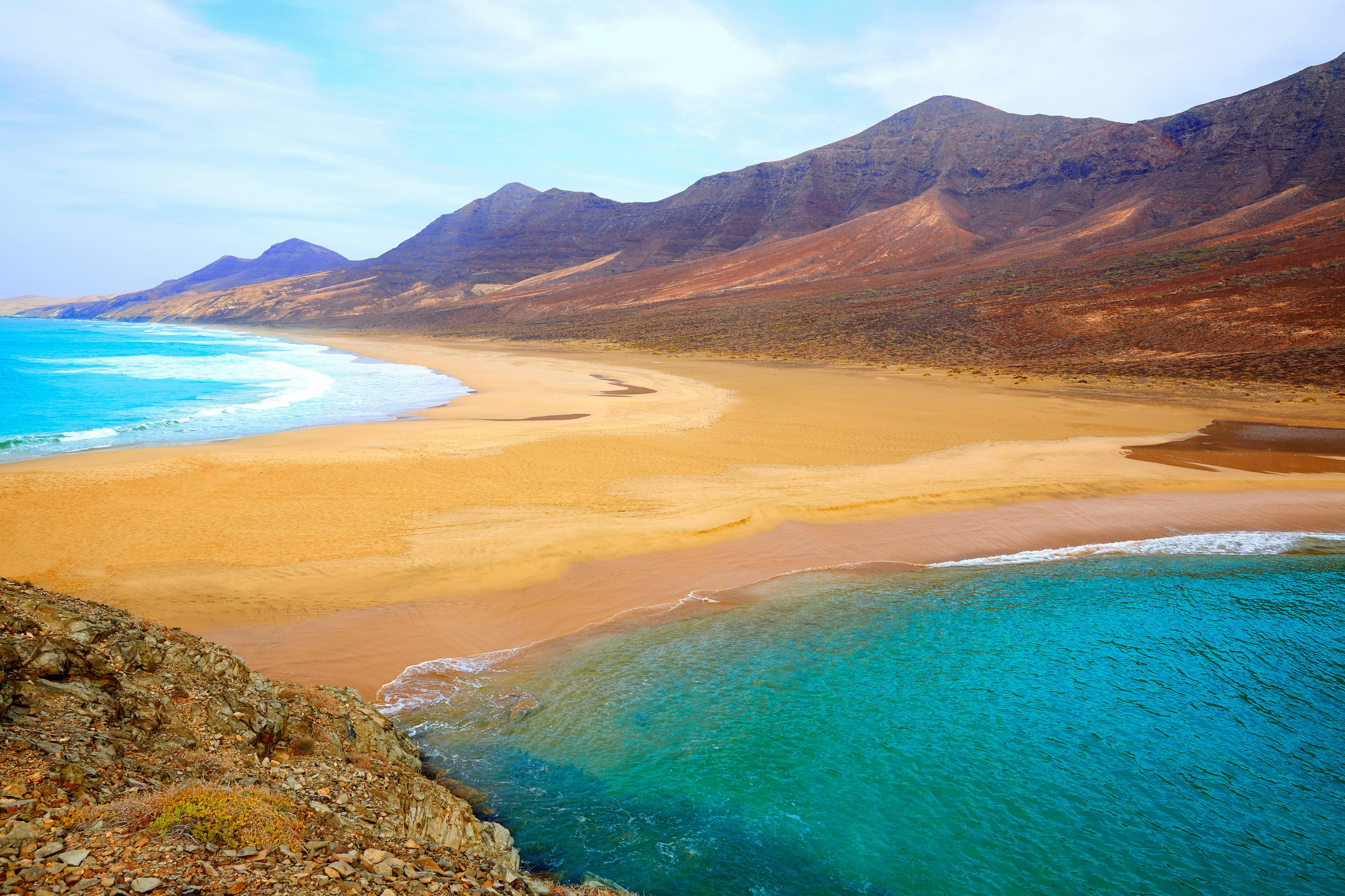 A golden stretch of sand is lapped on either side by azure water on Fuerteventura, Canary Islands