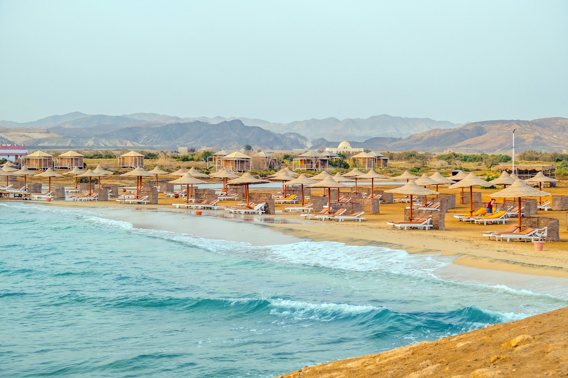 Loungers and umbrellas on a turquoise-water beach backed by orange mountains, Marsa Alam Egypt