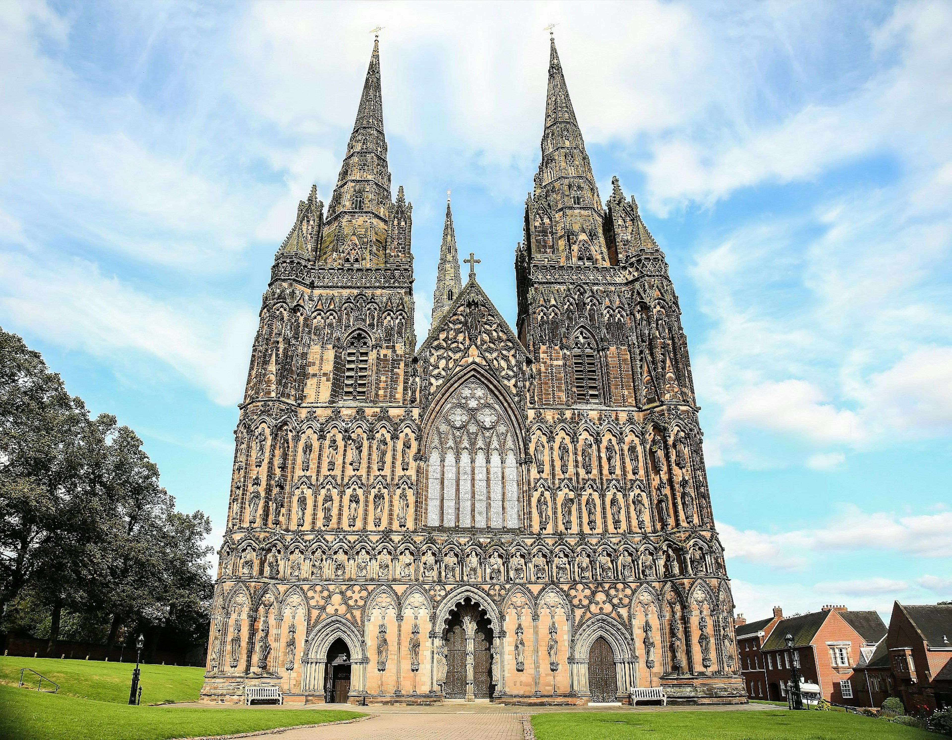 Looking up at the elaborate Gothic facade of a three-spired stone cathedral covered in statuary.