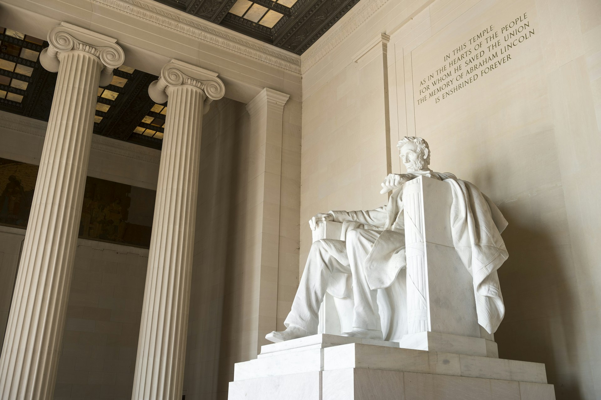 A vast white-stone sculpture of a man sat on a chair in a space with decorative columns. Text engraved into the wall above says  "In this temple as in the hearts of the people for whom he saved the Union, the memory of Abraham Lincoln is enshrined forever."