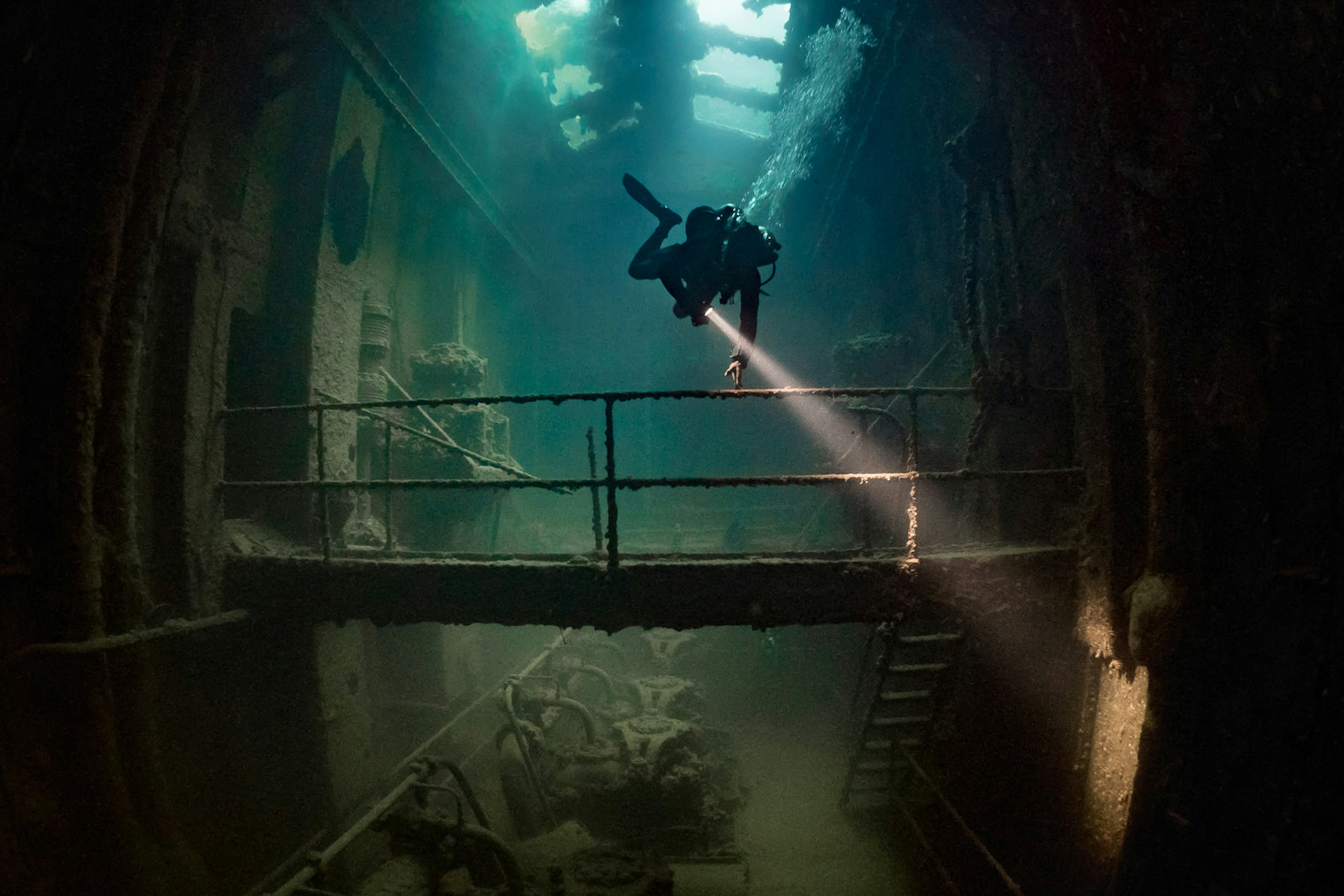 A diver investigates a shipwreck with torch in hand.