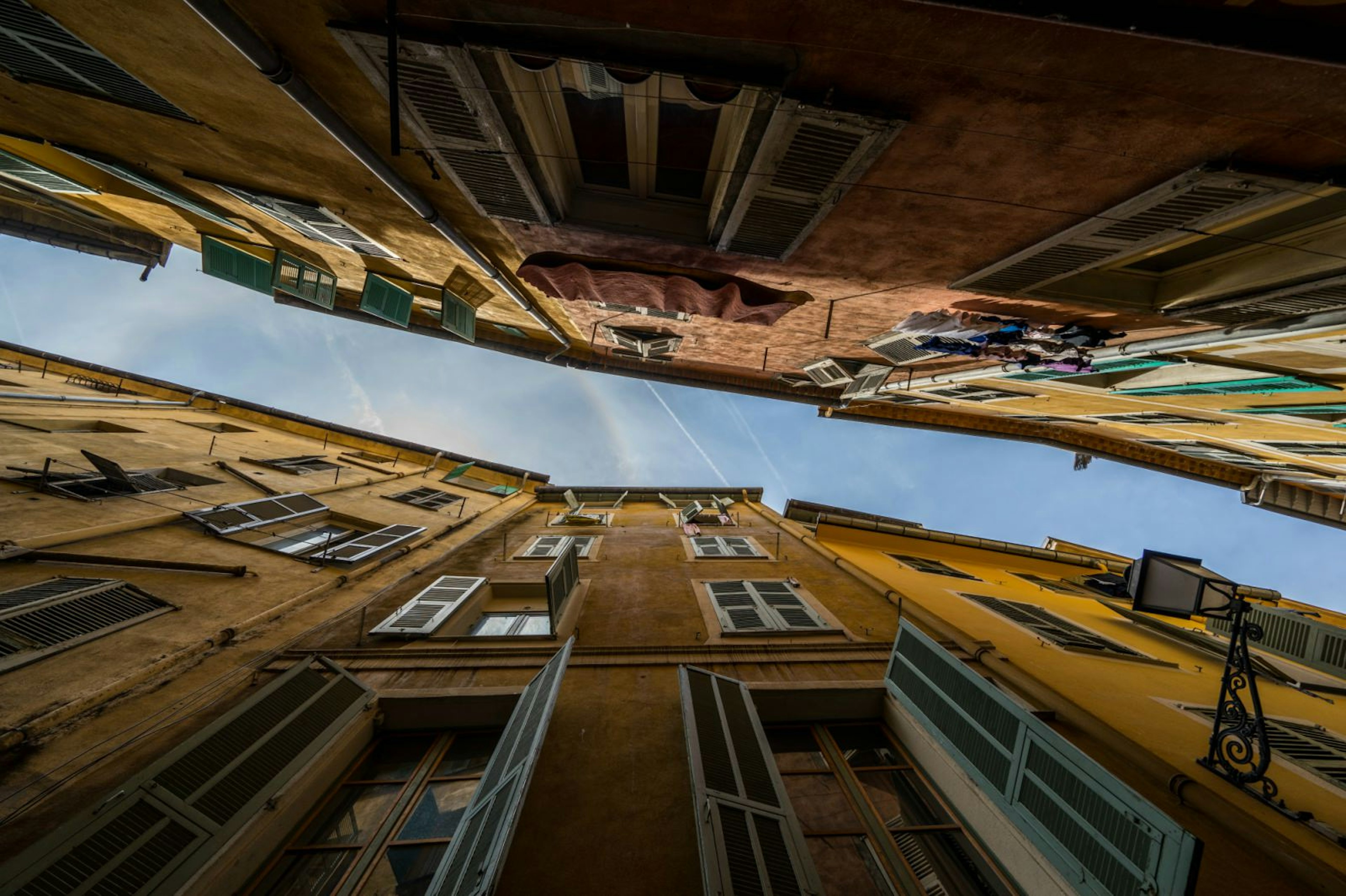 Looking up into the blue sky and old houses with open windows in the old town of Nice, France, standing in a narrow alley