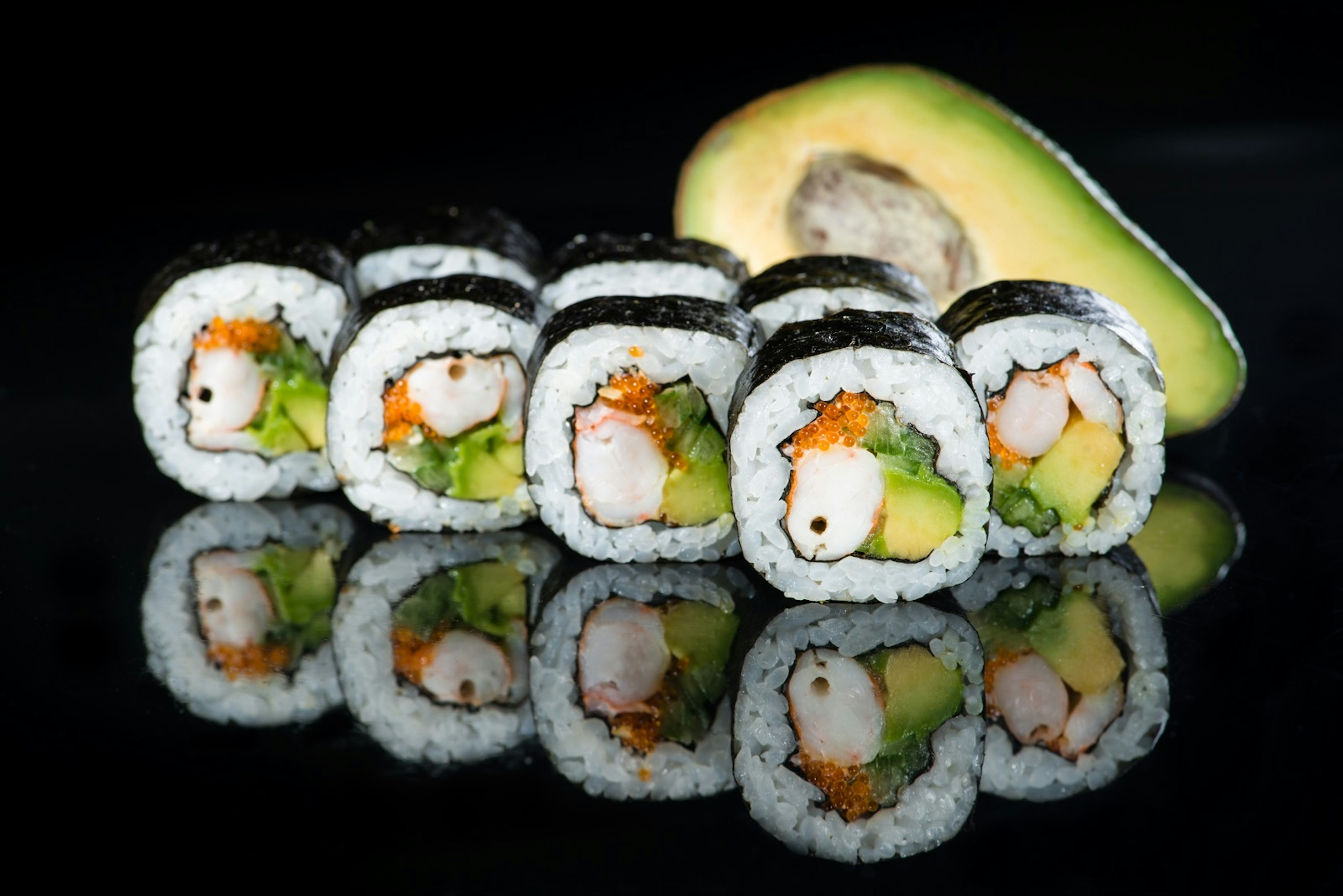 Fresh delicious Japanese sushi with avocado, cucumber, shrimp and caviar on dark background; California roll