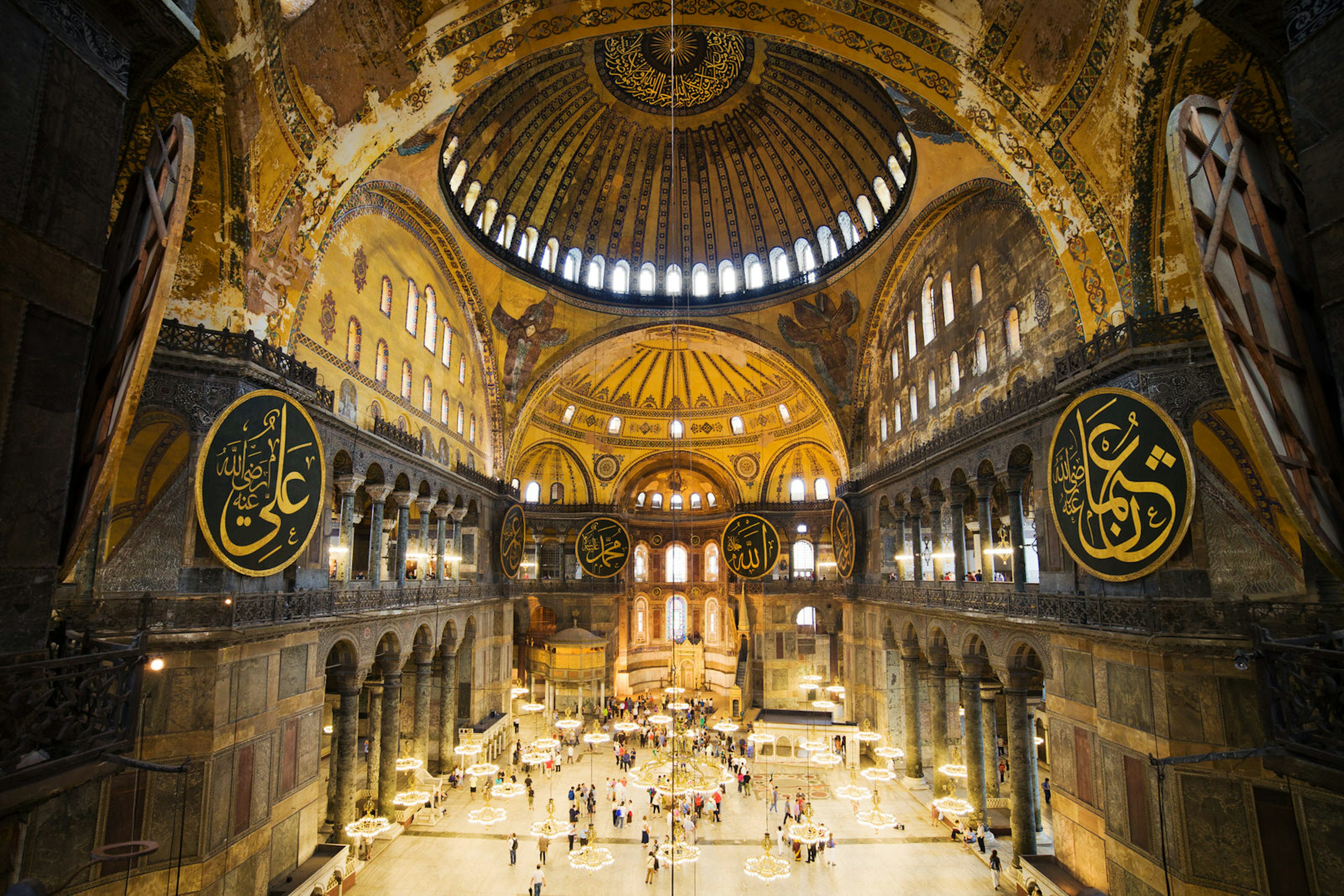 A vast space with a dome covered in murals and Arabic writing