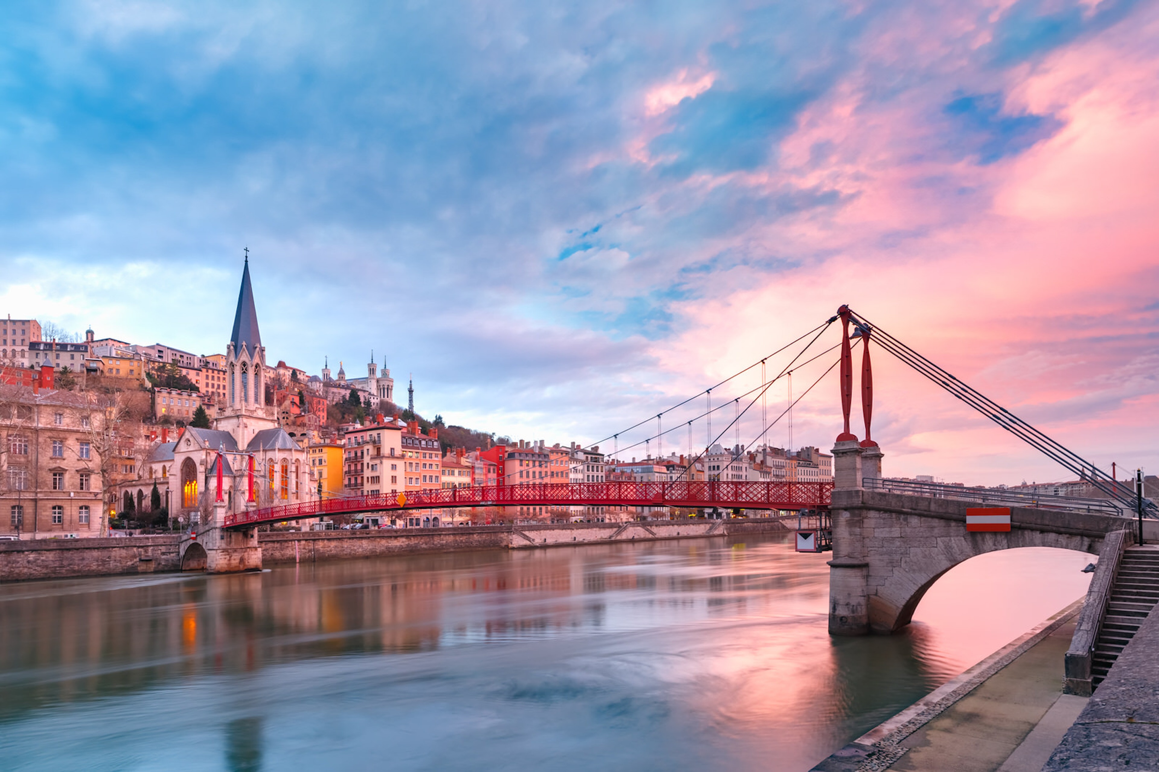 Saint Georges church and a footbridge across Saône river in Lyon's Old Town during sunset with a pink and blue sky