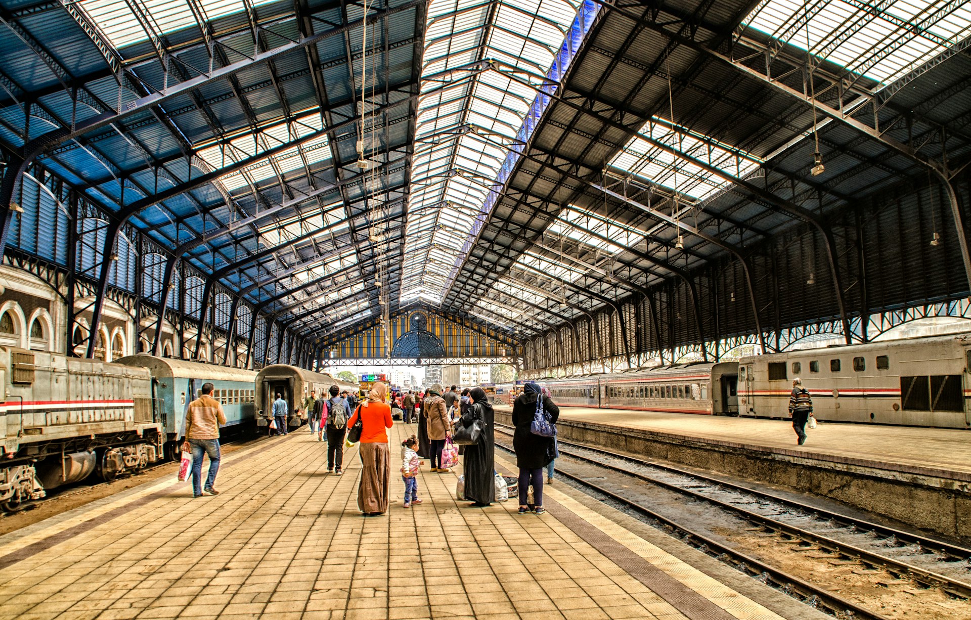 A group of travelers make their way along a train platform in a station with a glass and steel roof