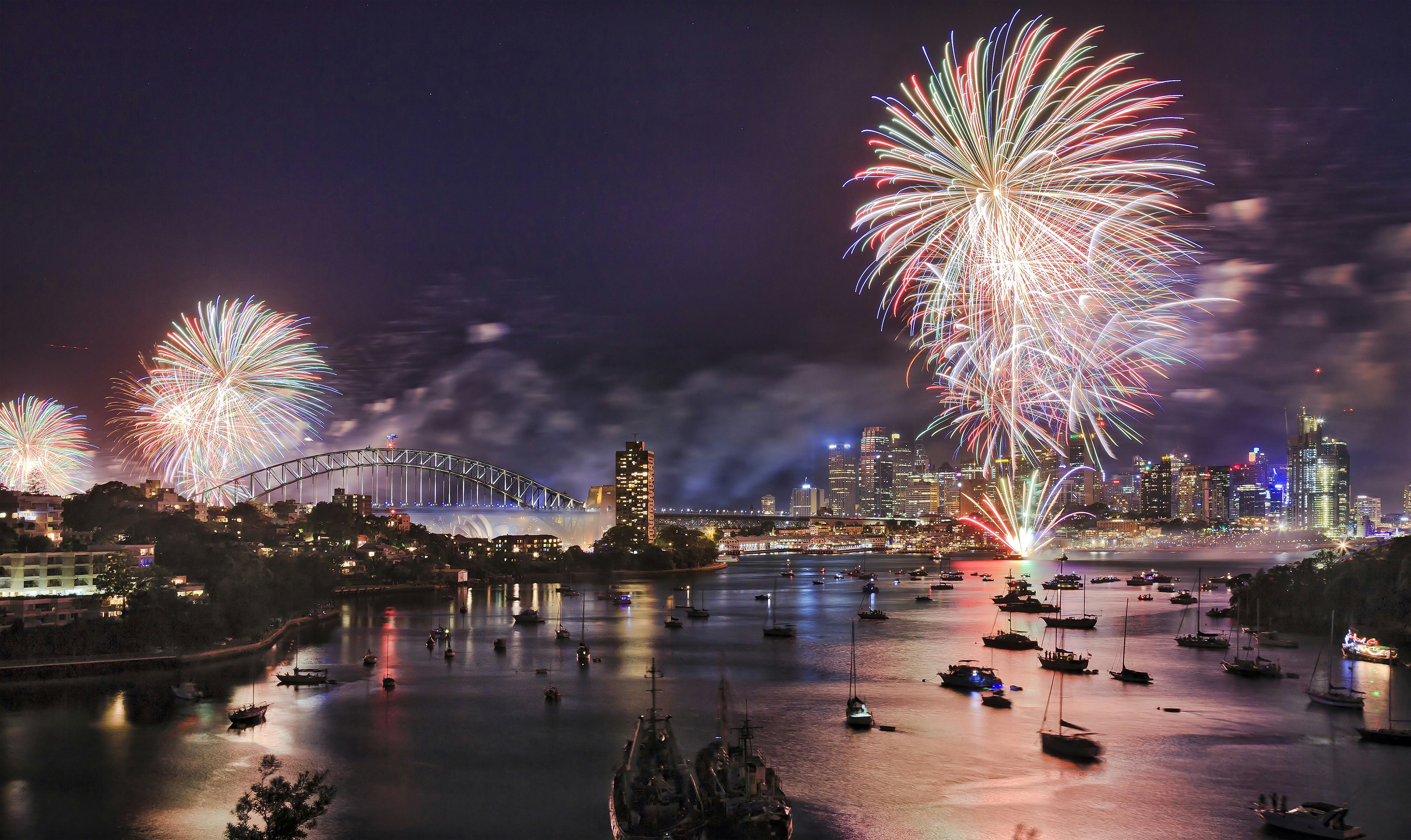 New Year's Eve fireworks explode over a harbour city with boats moored nearby