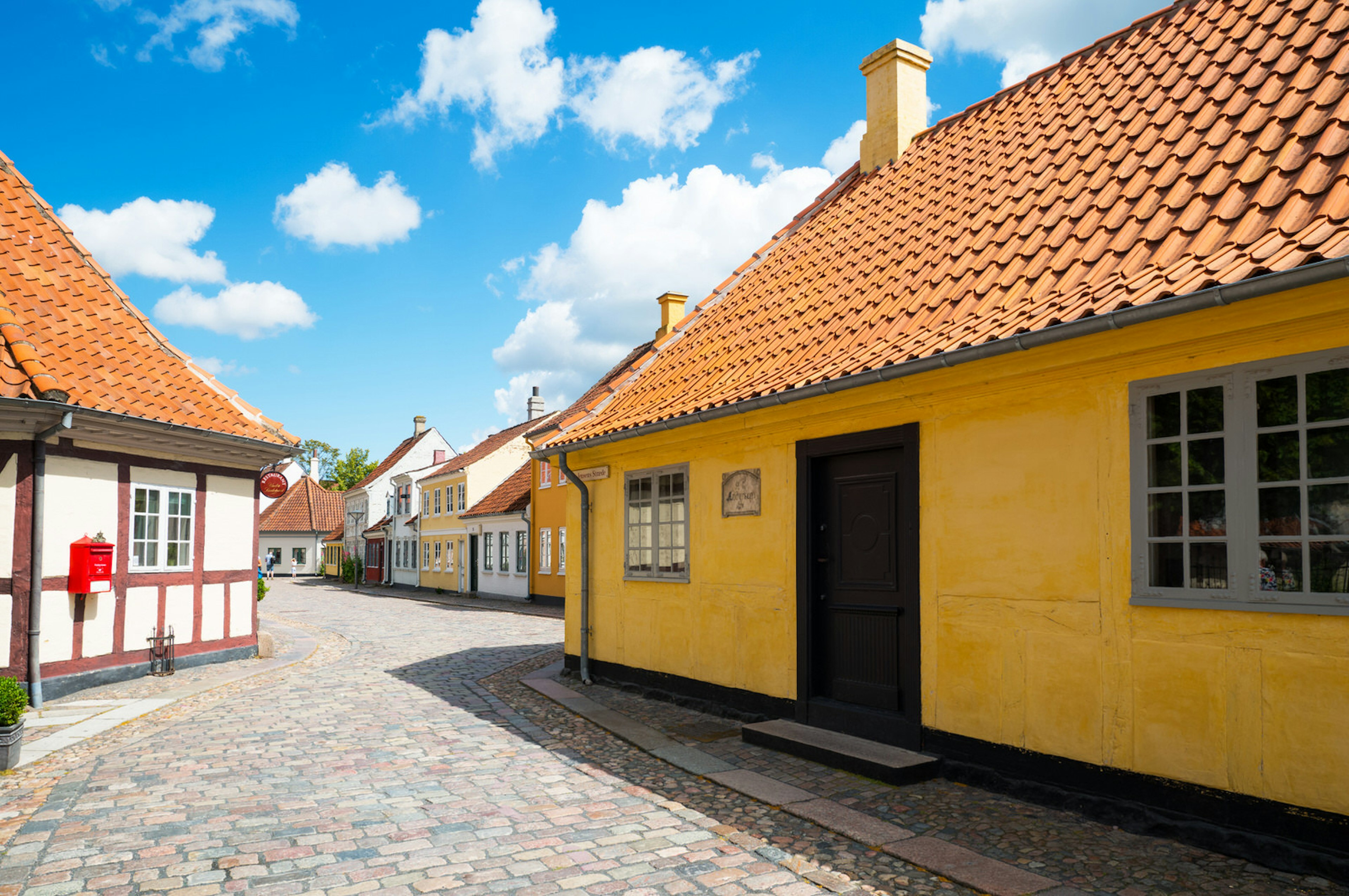 Hans Christian Andersen's birthplace is a single-storey traditional house with yellow exterior walls and steep terracota-tiled roof; the street outside it is cobbled