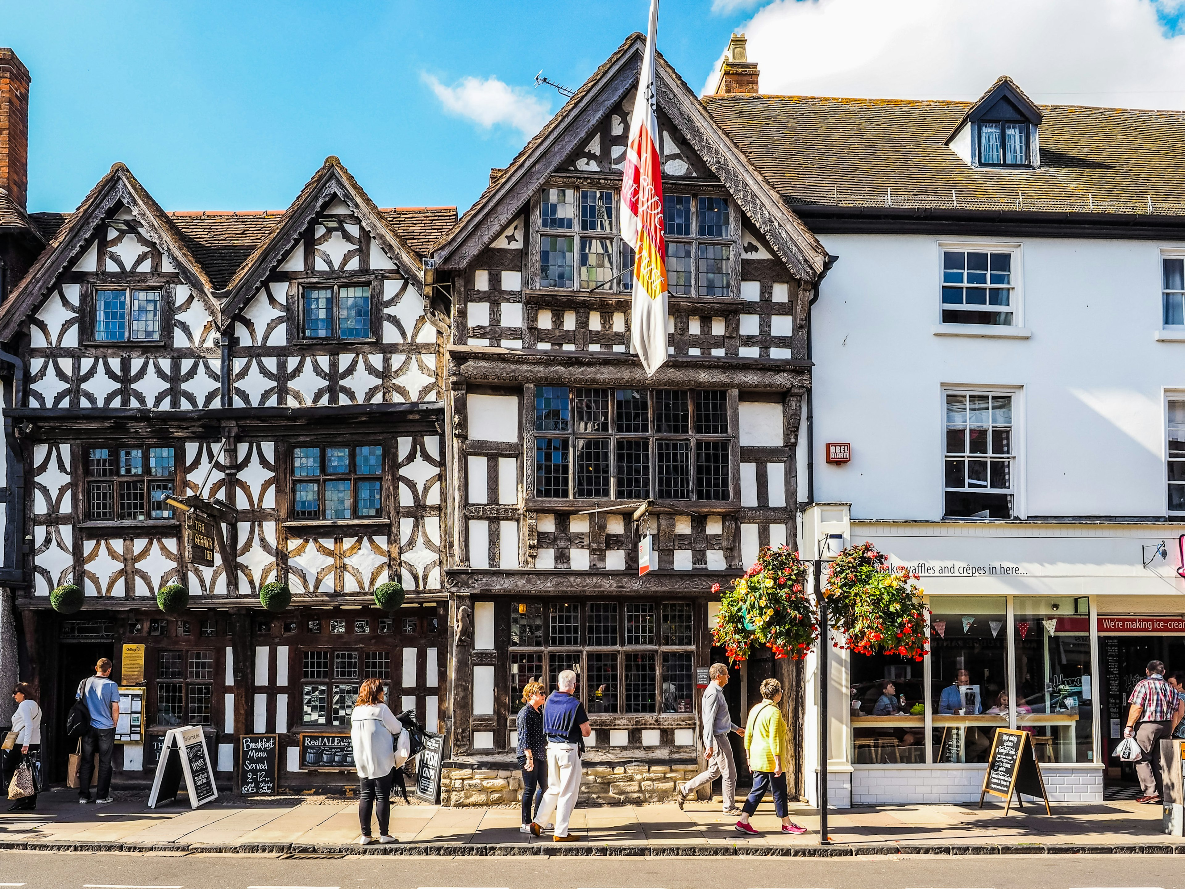 A Tudor building in Stratford-upon-Avon, having a black and white appearance due to its exposed wooden frames; it houses a restaurant, while there is another next door in a more modern building.