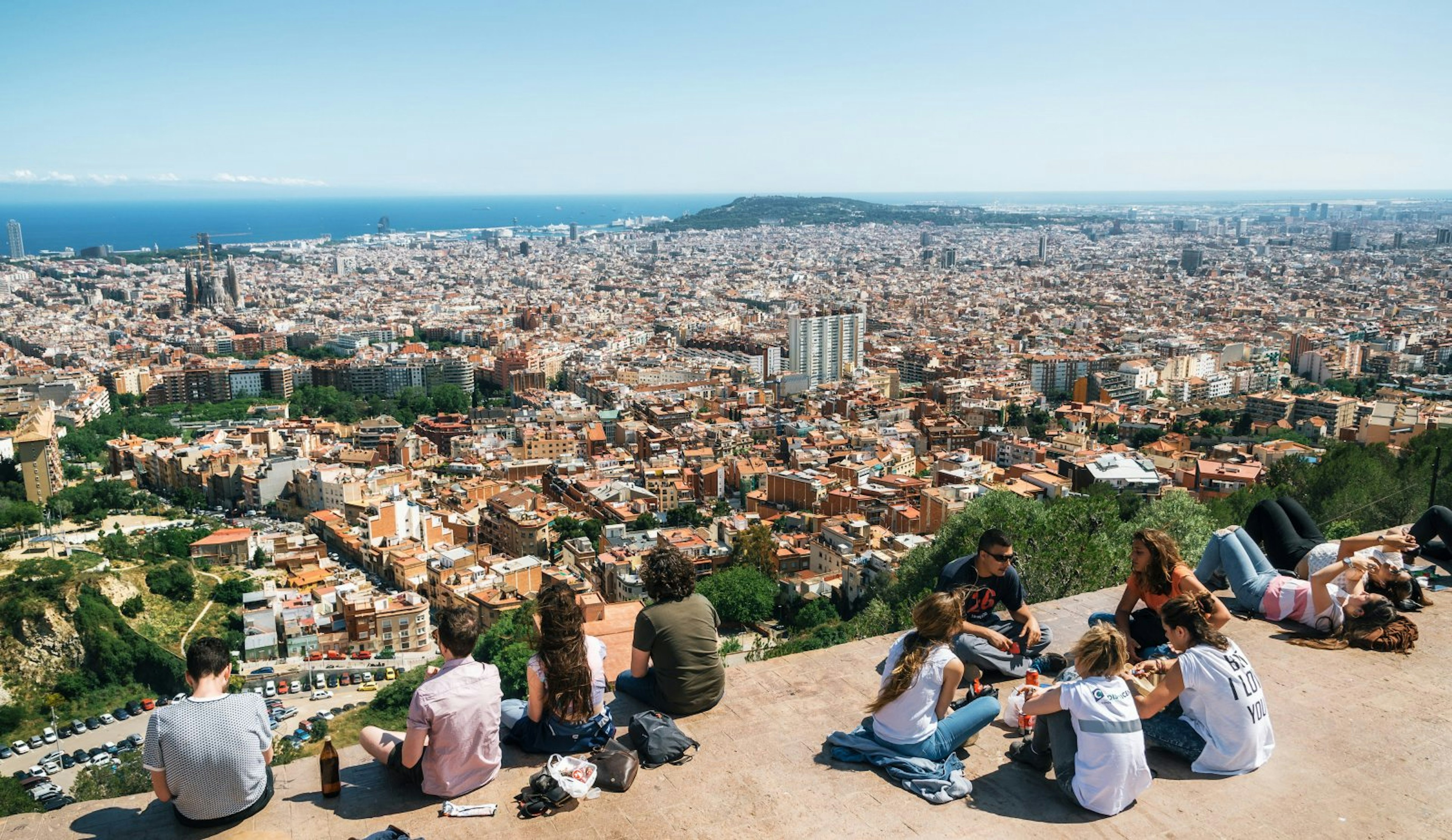 Teens sit on the viewpoint with a view of the city of Barcelona stretching off into the distance