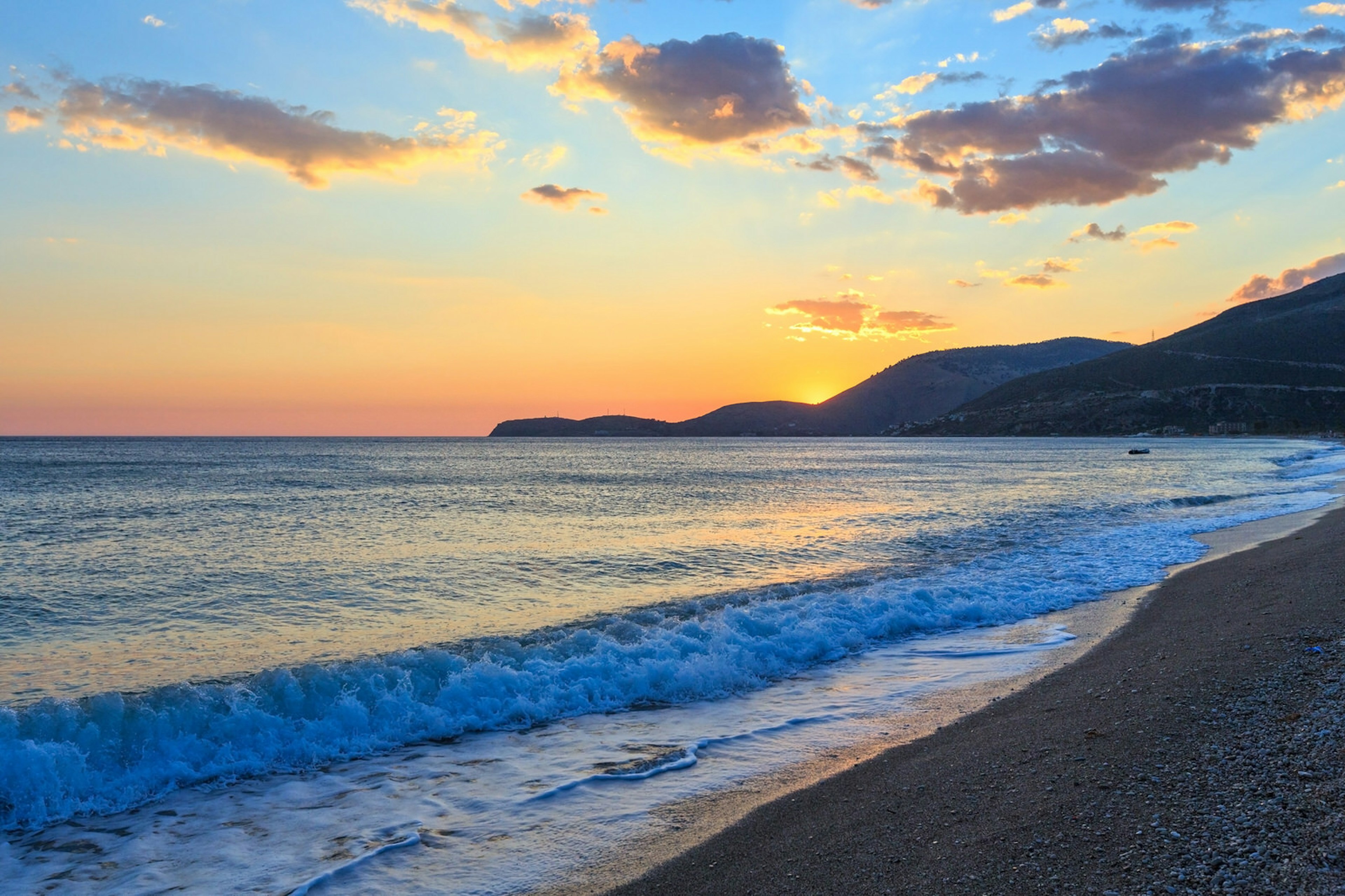 Sunset on Borsh beach with the sun setting behind mountains in the background with the tide gently lapping the shore