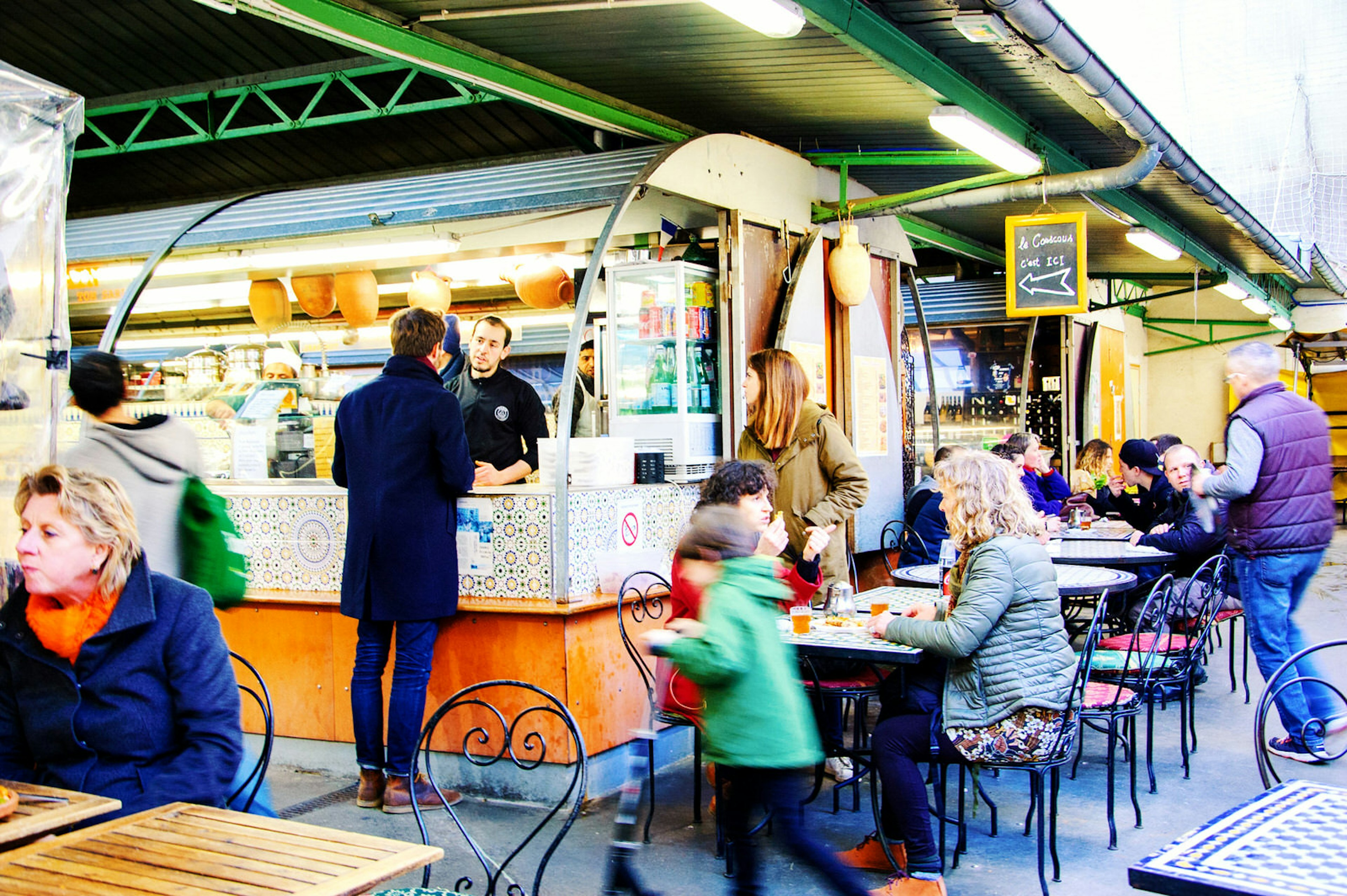 People sit at tables eating food bought from the nearby market stalls