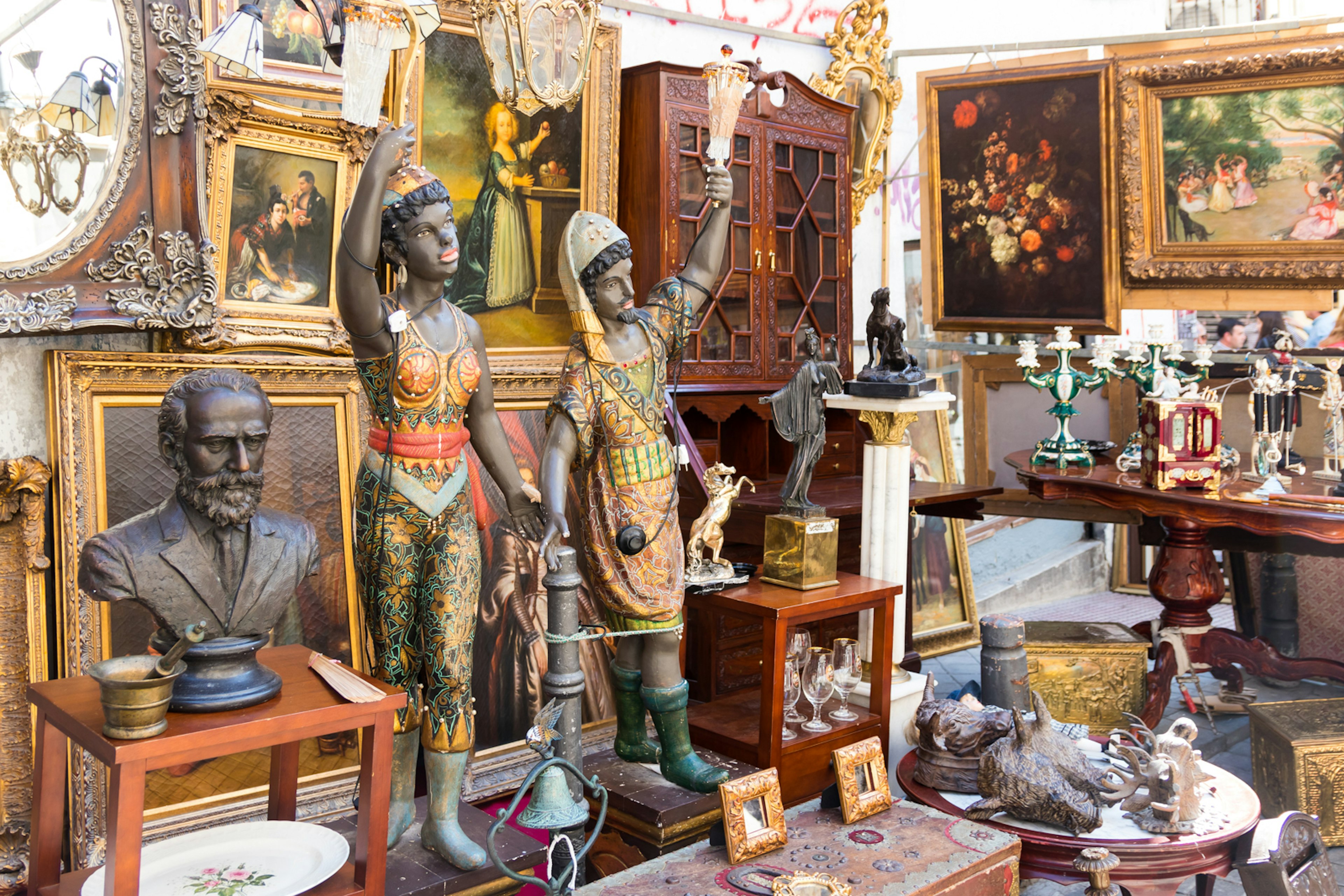 Antique shop in El Rastro flea market, including two figures and a bronze bust with several paintings on the wall behind; free things to do in Madrid