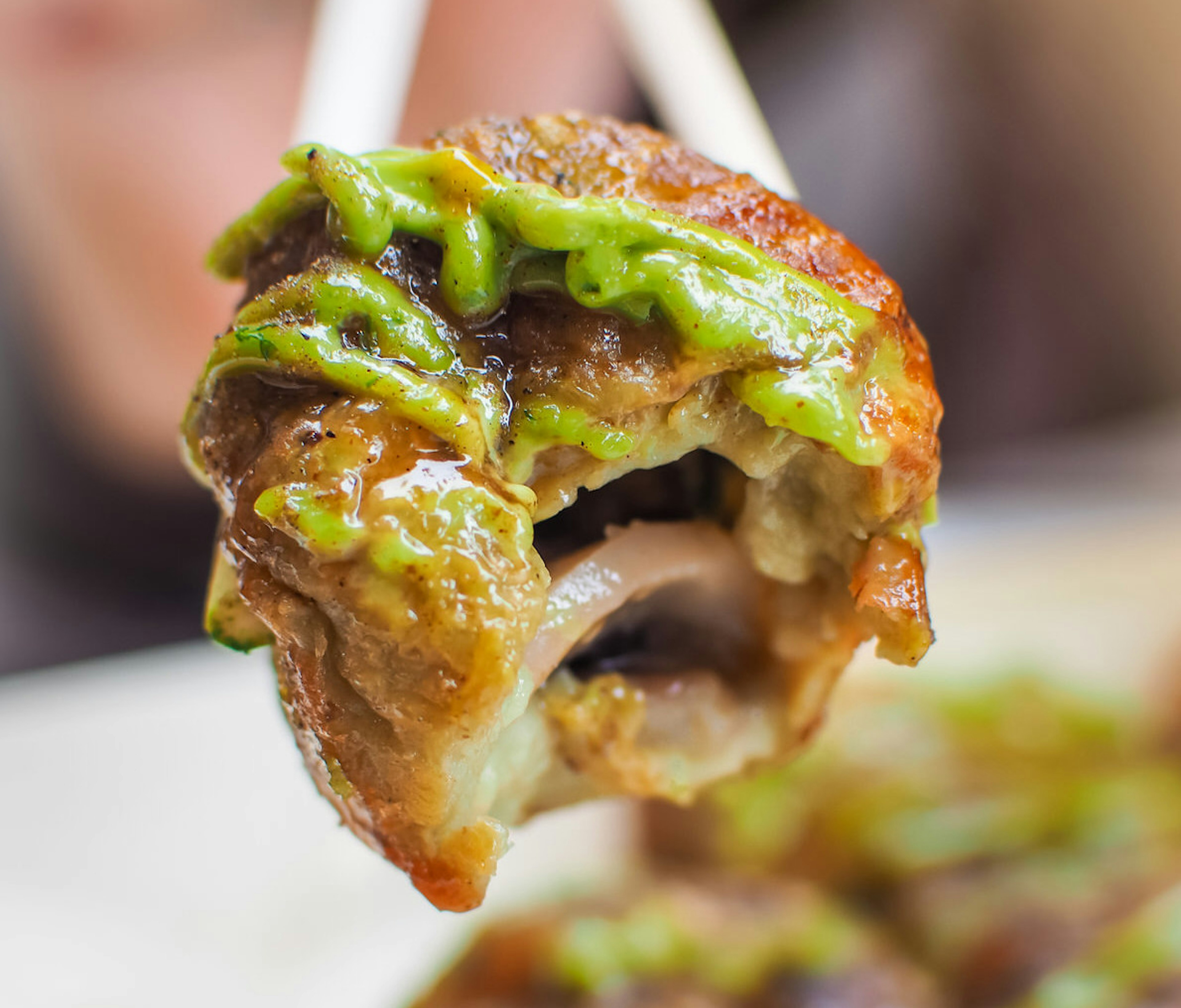 A diner raises a tako-yaki (octopus ball) over their plate with chopsticks