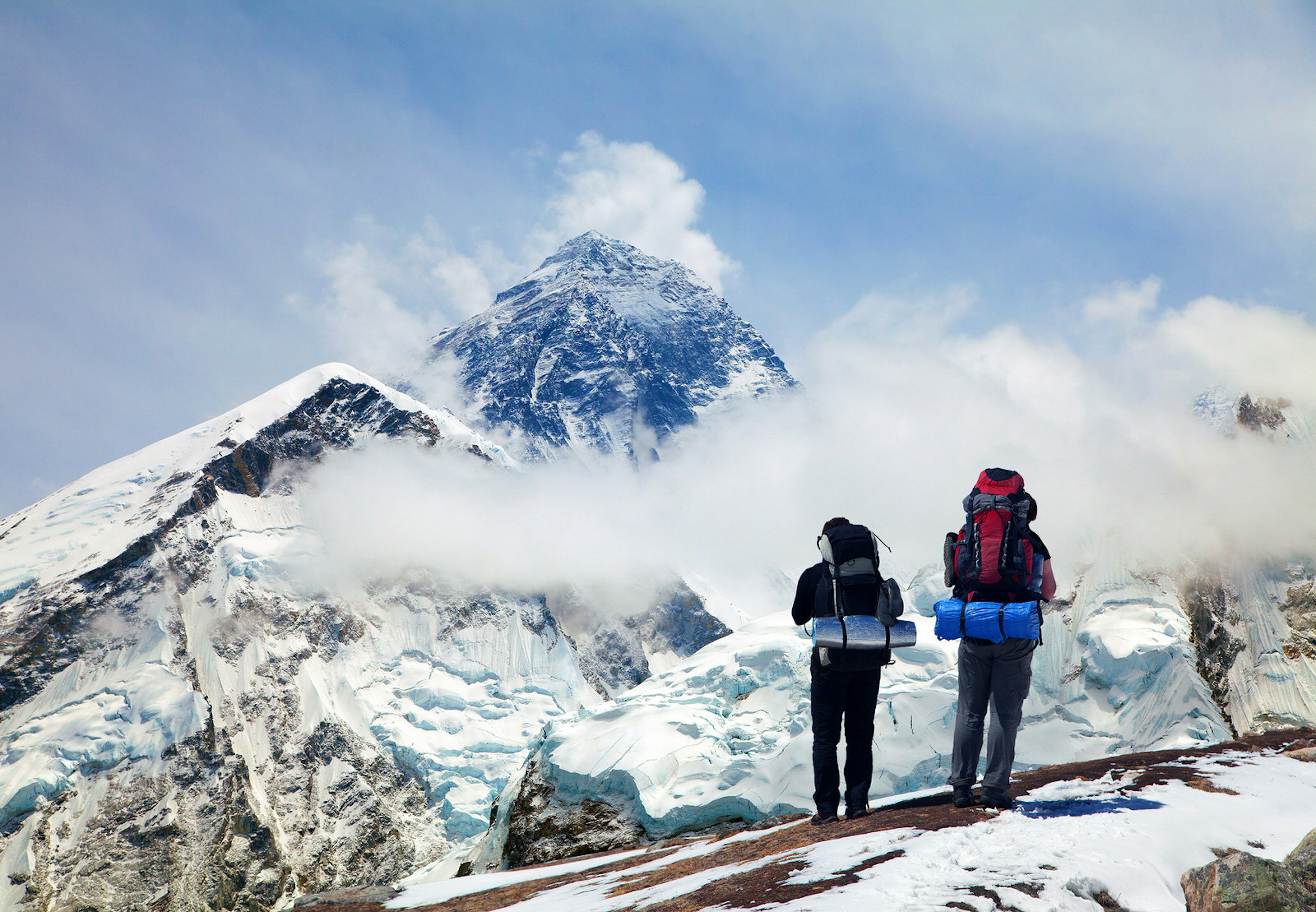 Snow-covered Mount Everest seen from Kala Patthar with two tourists carrying large backpacks