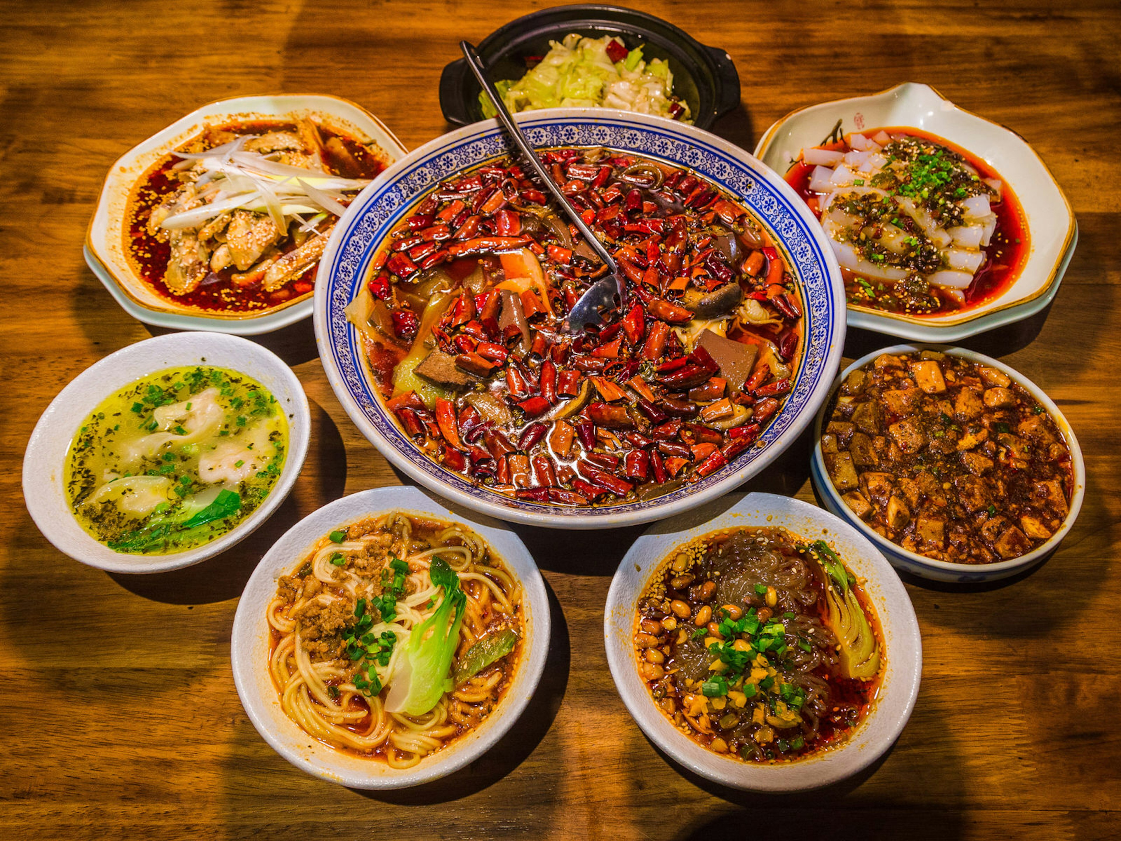 Bowls of different Sichuan foods, including a bowl of red chilli peppers in the middle, and some bowls of noodles. Sichuan is known for its spicy, tongue-numbing peppercorns and chillis ? HelloRF Zcool / Shutterstock