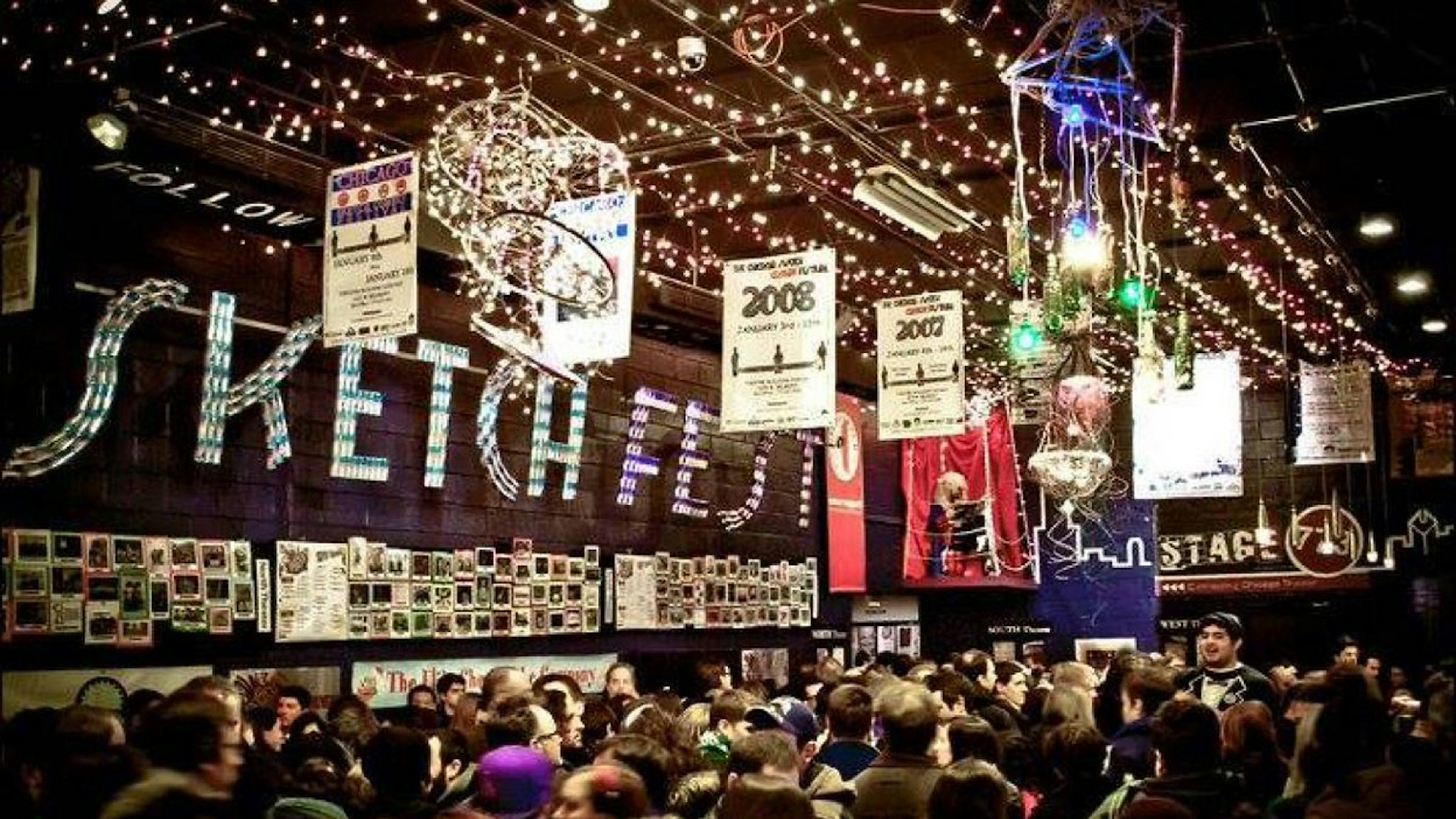 fairy lights and banners deck a high ceiling above a crowd of people gathered for Sketchfest