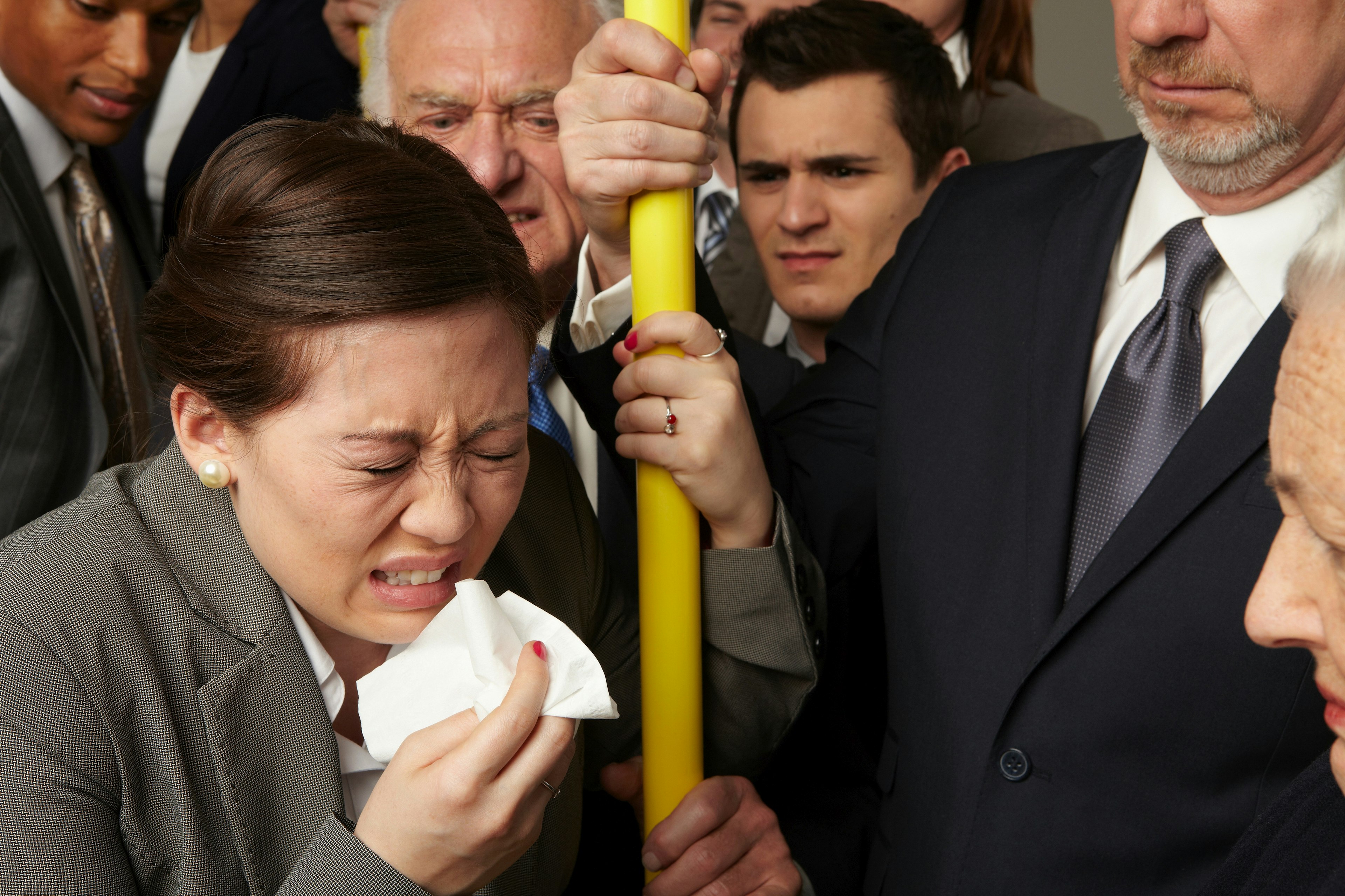 A woman sneezing on a bus while other passengers look on in disgust