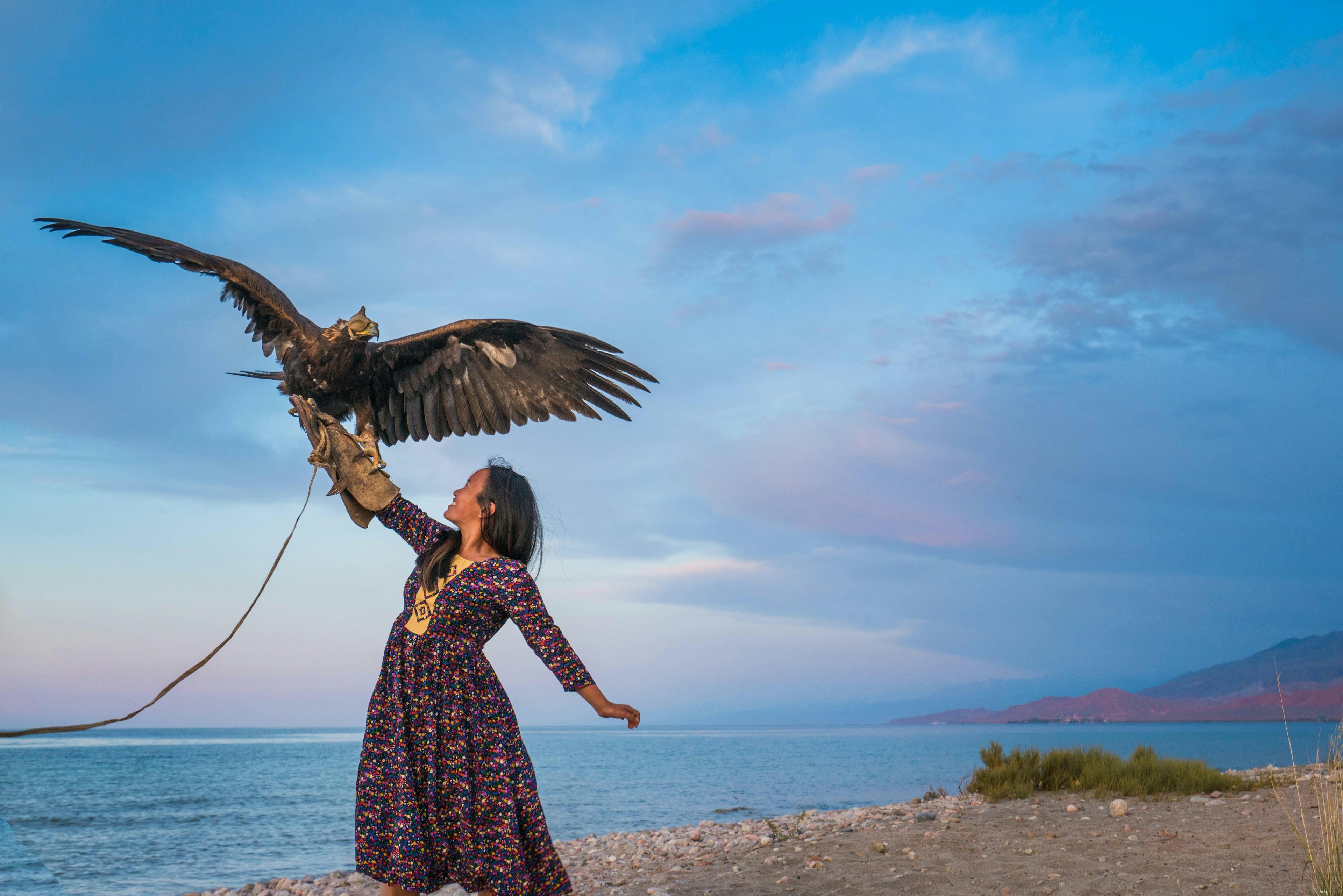 The writer wears a thick falconry glove, with an eagle resting on her hand. A lake is in the background