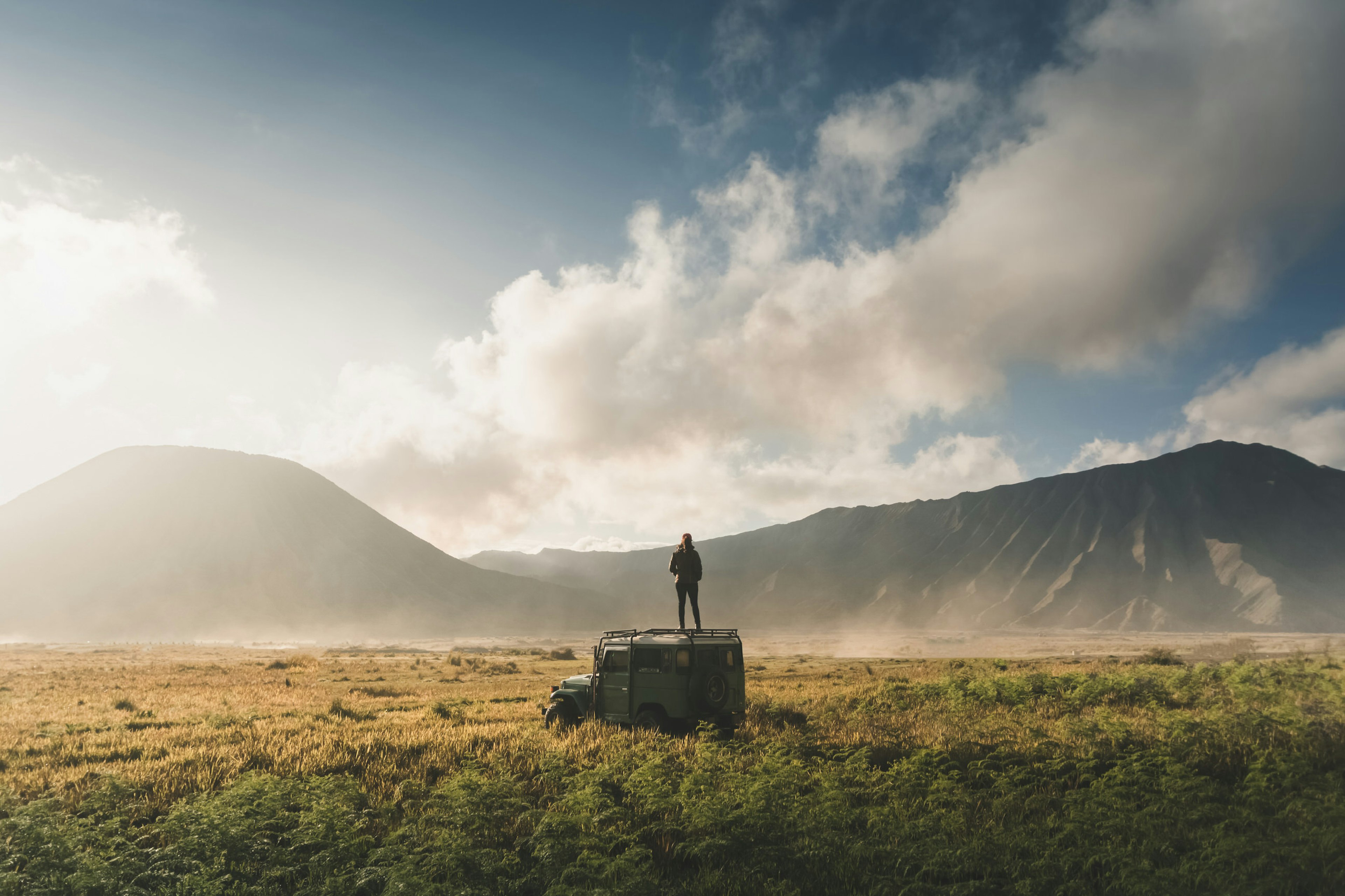 A woman stands on top of a jeep in a field near Mt Bromo in Indonesia.