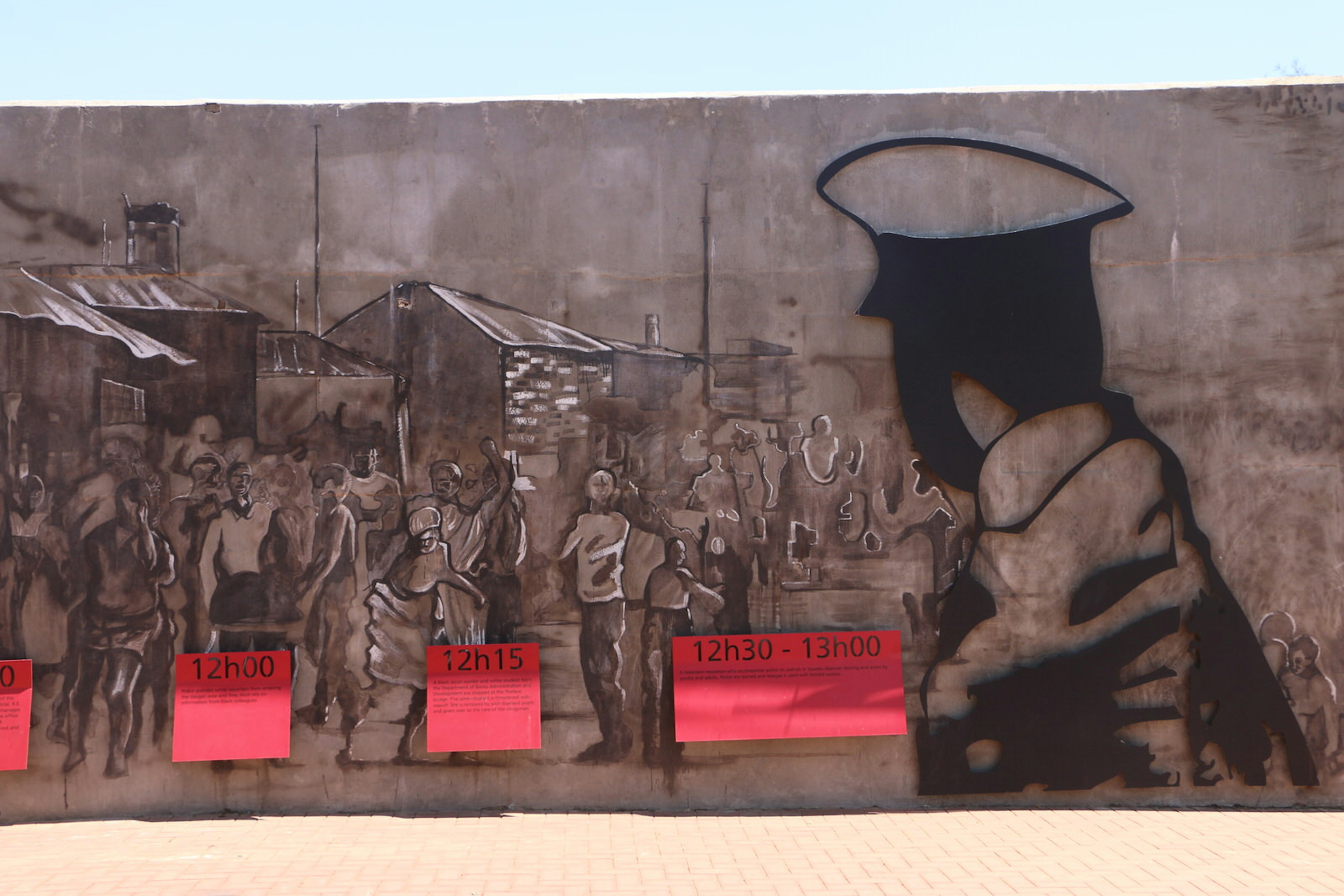 A dark, sepia-coloured mural of a scene from the June 16 protest. A policeman's head in the foreground is turned towards a street crowded with protestors and lined with simple shelters © Simon Richmond / Lonely Planet