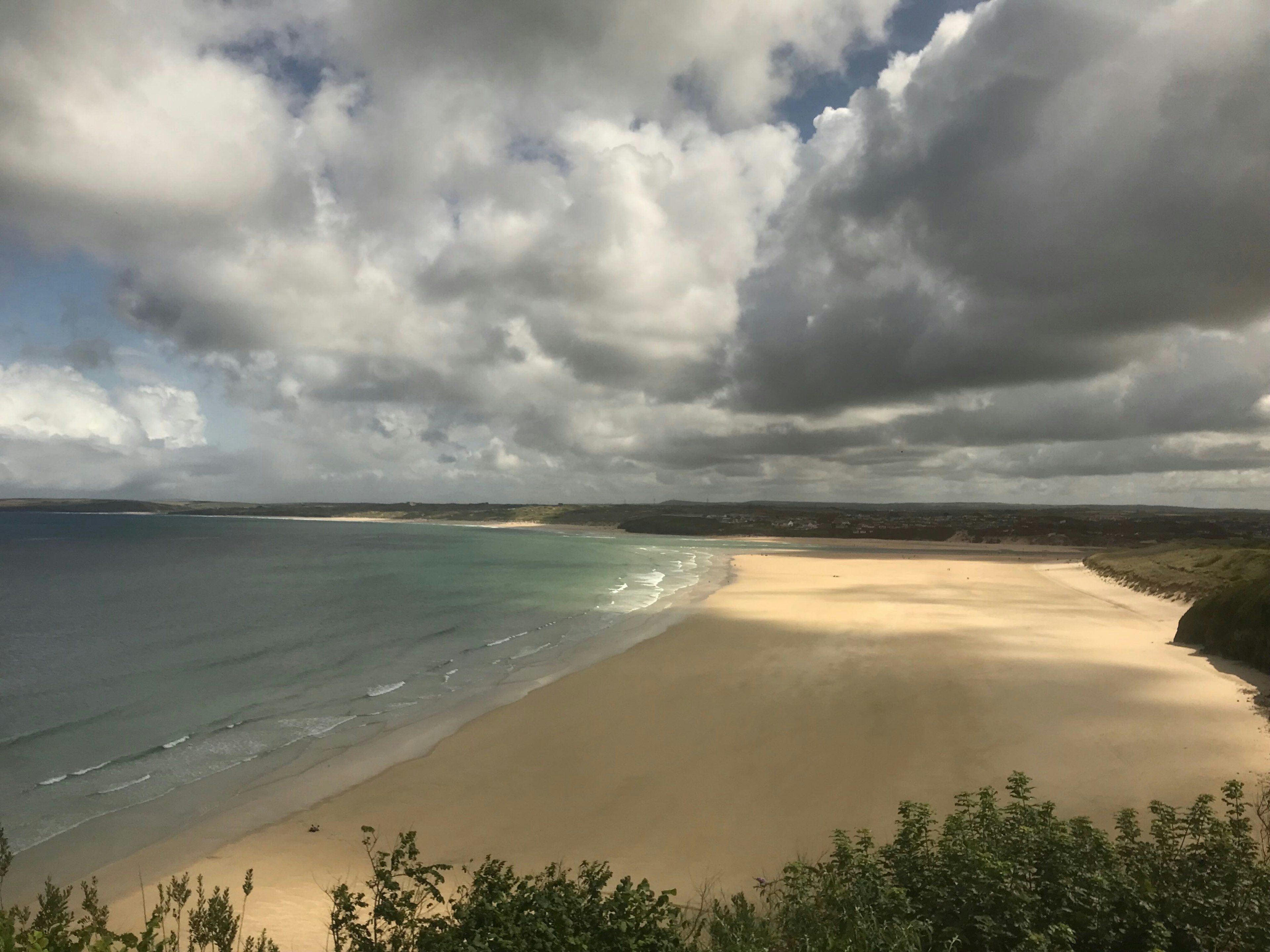 An empty, golden-sand beach with shadows on the sand from the clouds overhead