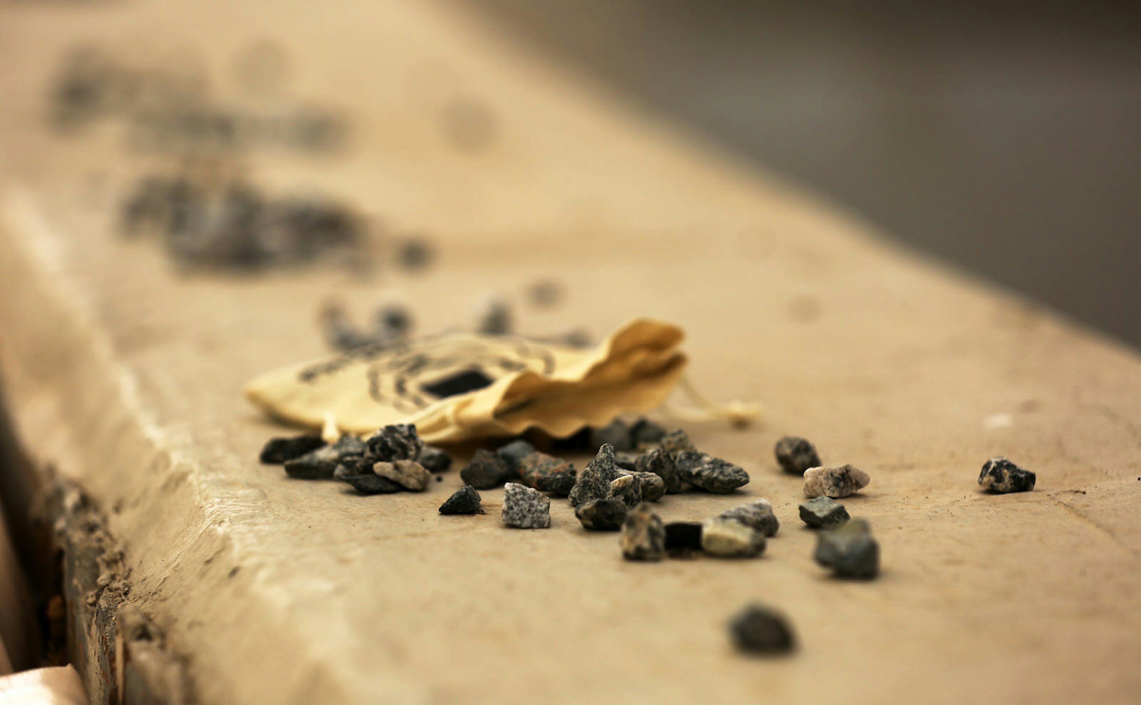 A pile of small pebbles sits next to a crumpled piece of yellowish paper on a concrete wall.