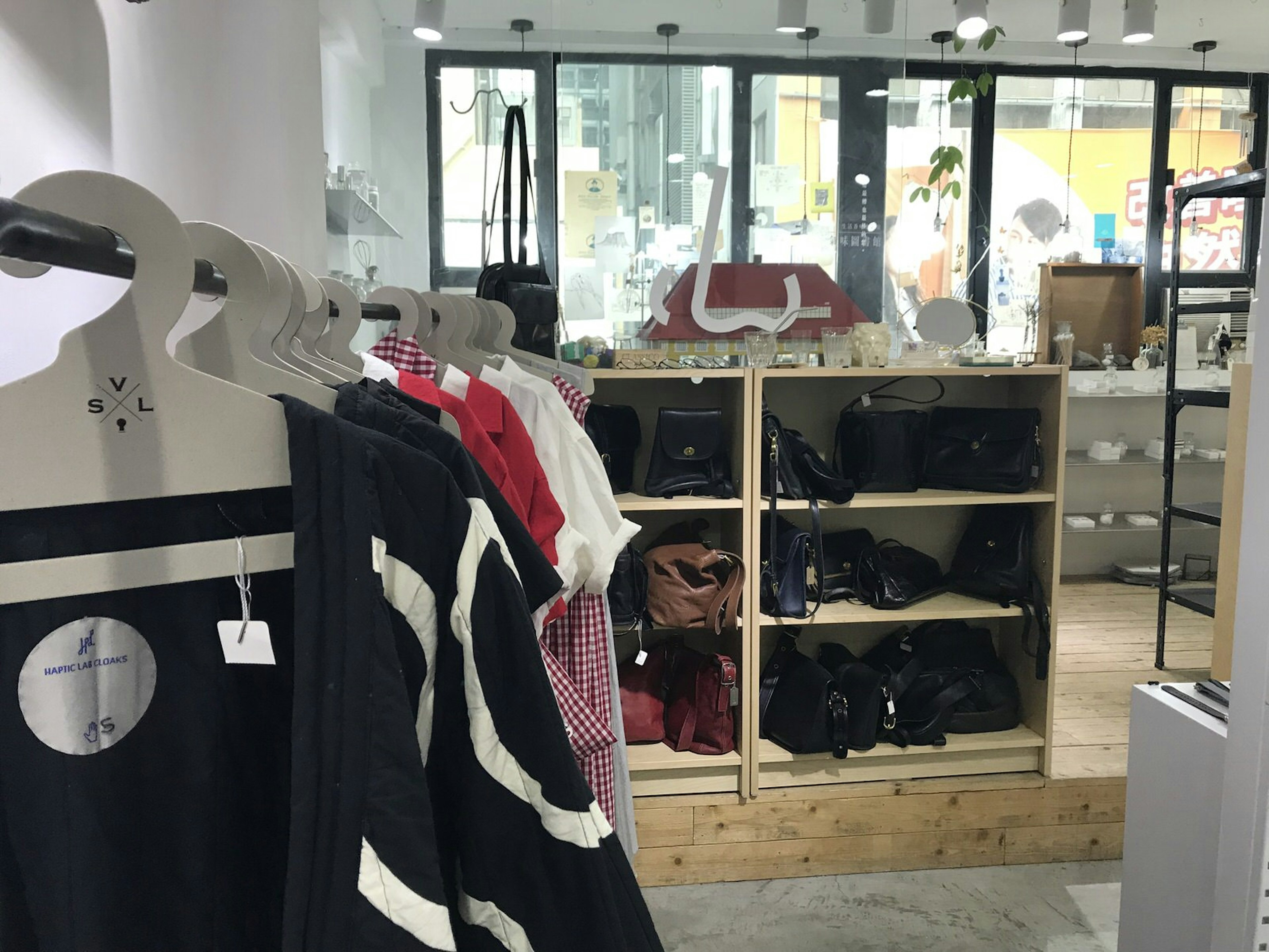 A selection of clothing on hangers in the foreground and a shelf of bags and purses in the background