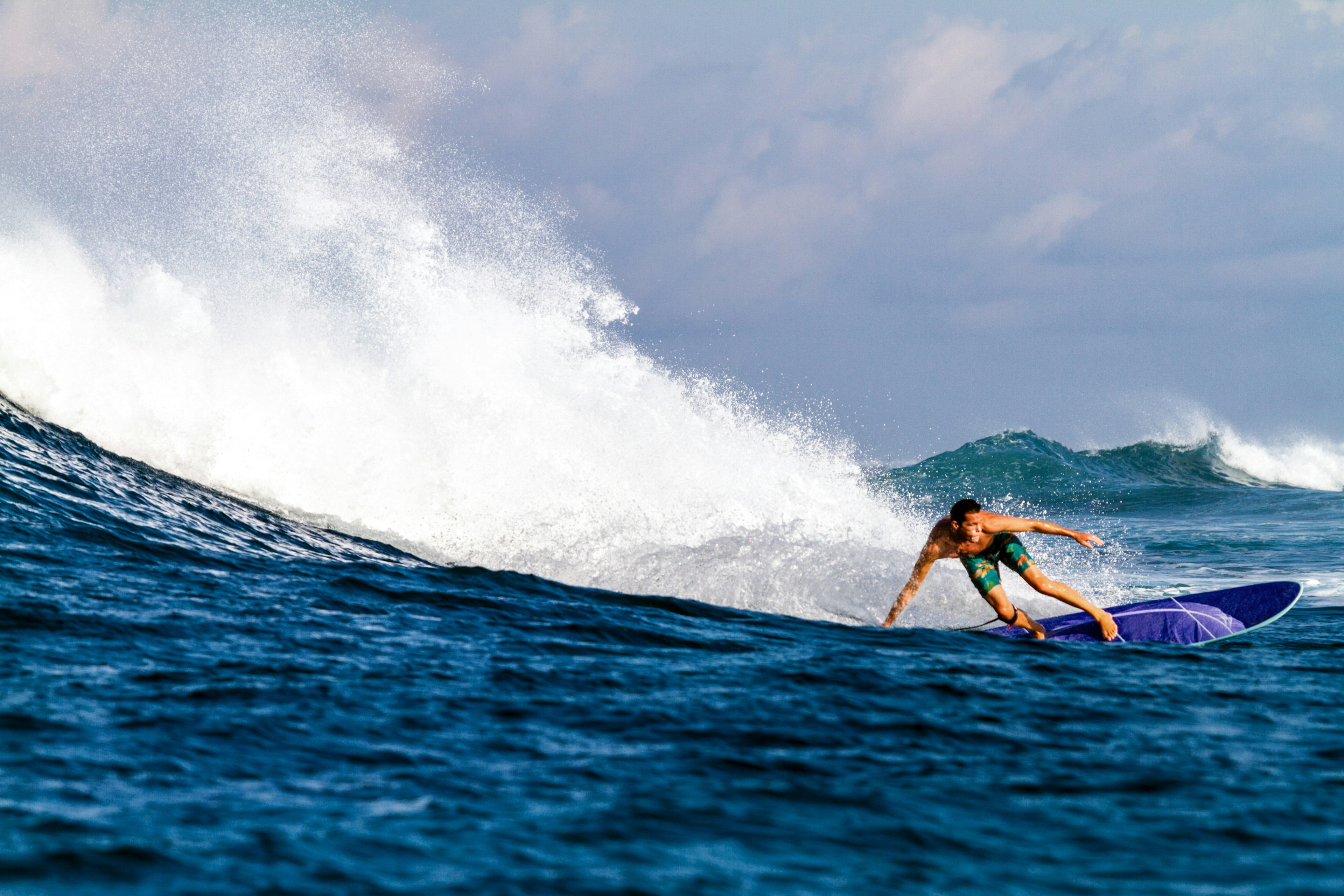 A surfer makes an impressive turn, with one hand skimming the surface of the water, with more waves crashing in the distance.