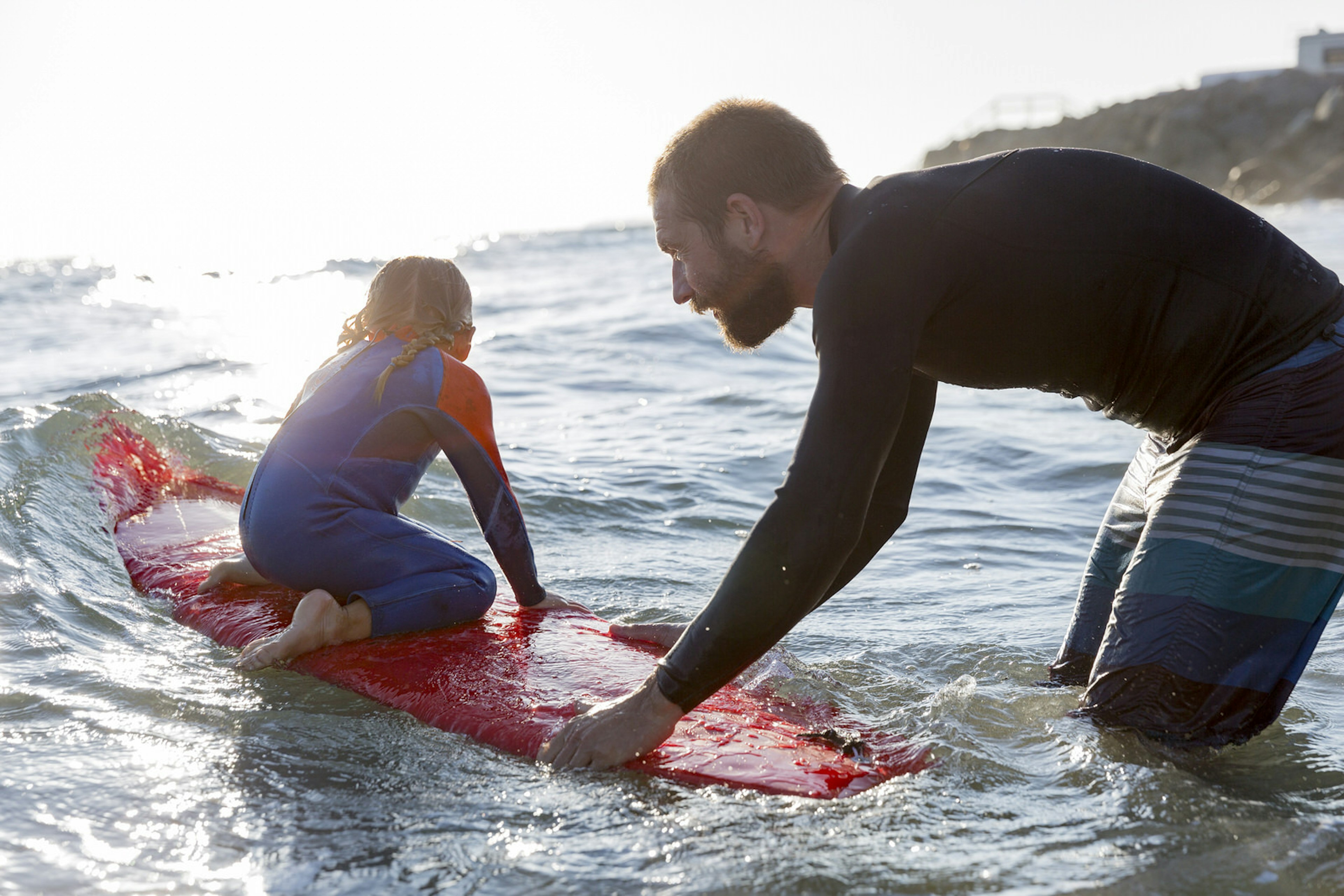 A Father pushes his little daughter into a wave on a surfboard.