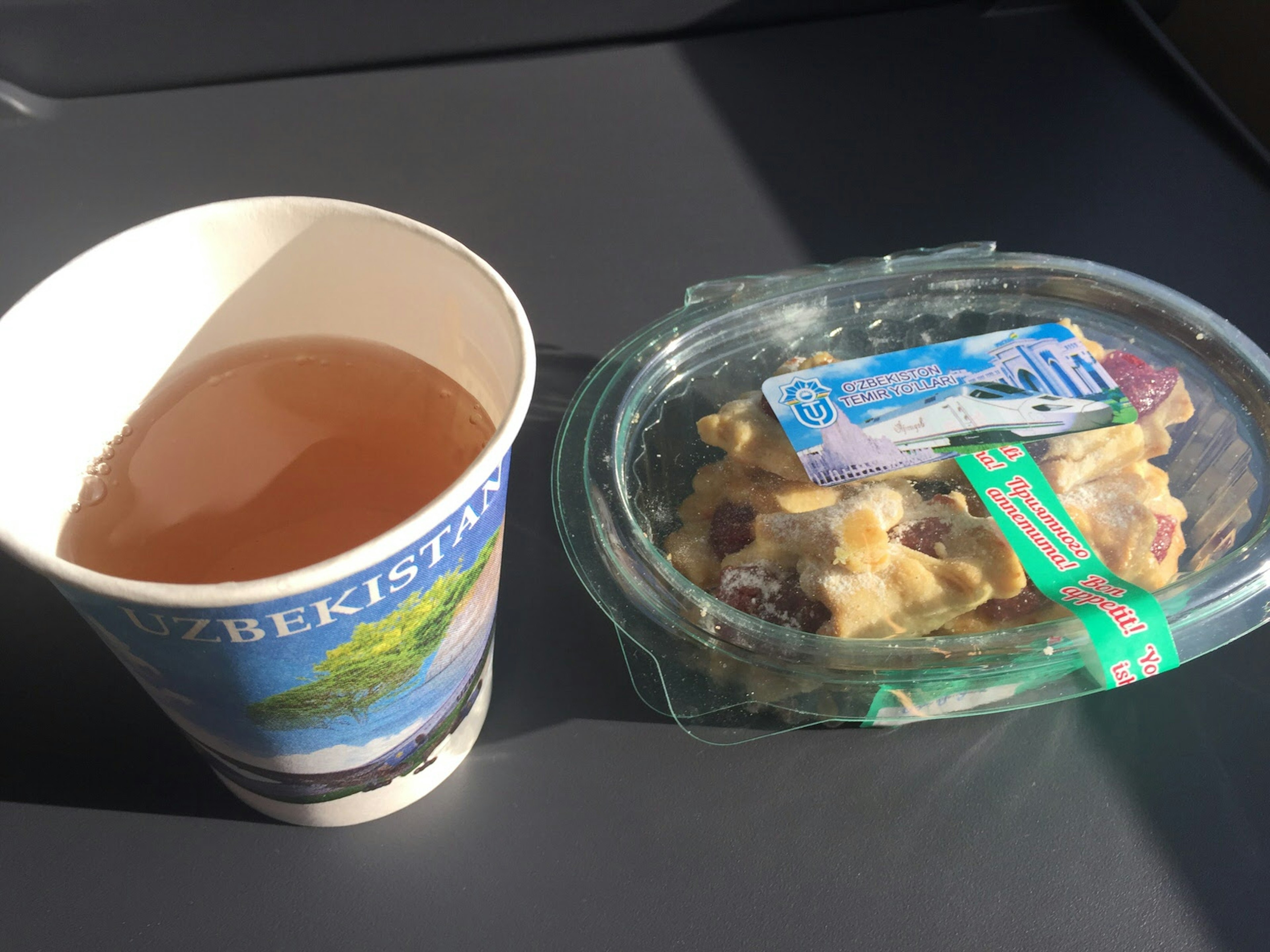 Cup of tea and a plastic container of jam biscuits on a train tray table