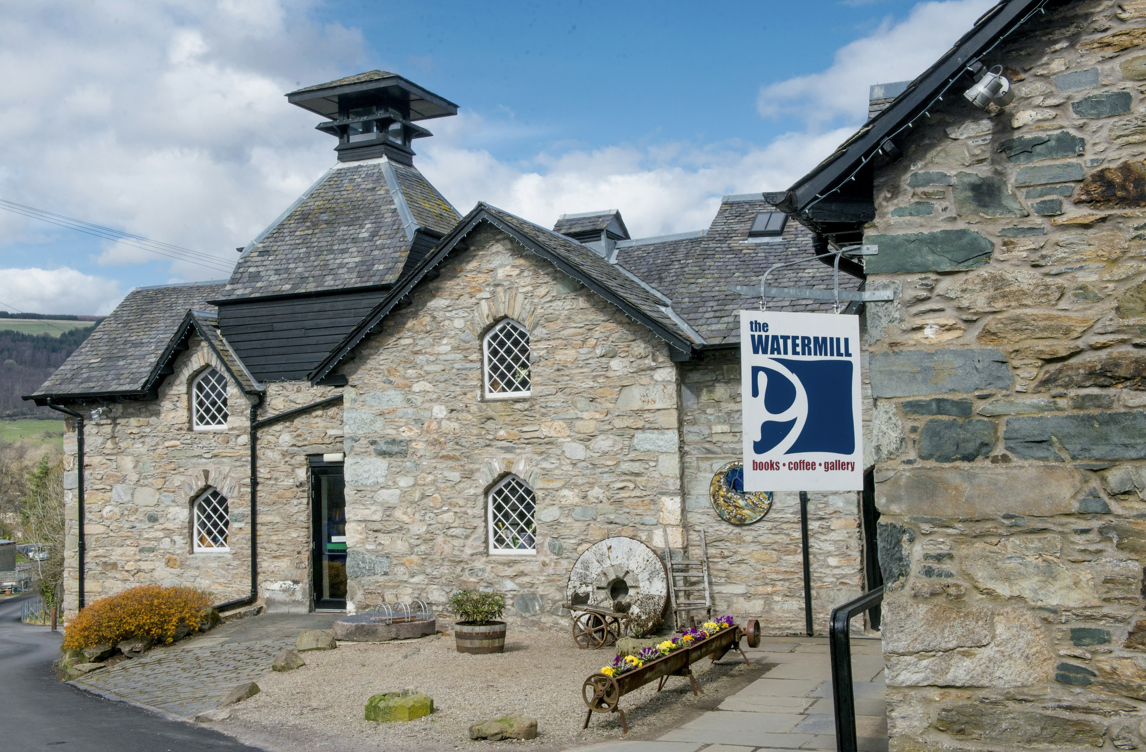 The exterior of the traditional stone watermill building in Aberfeldy, Perthshire. It has a pyramid-shaped turret and lattice windows.