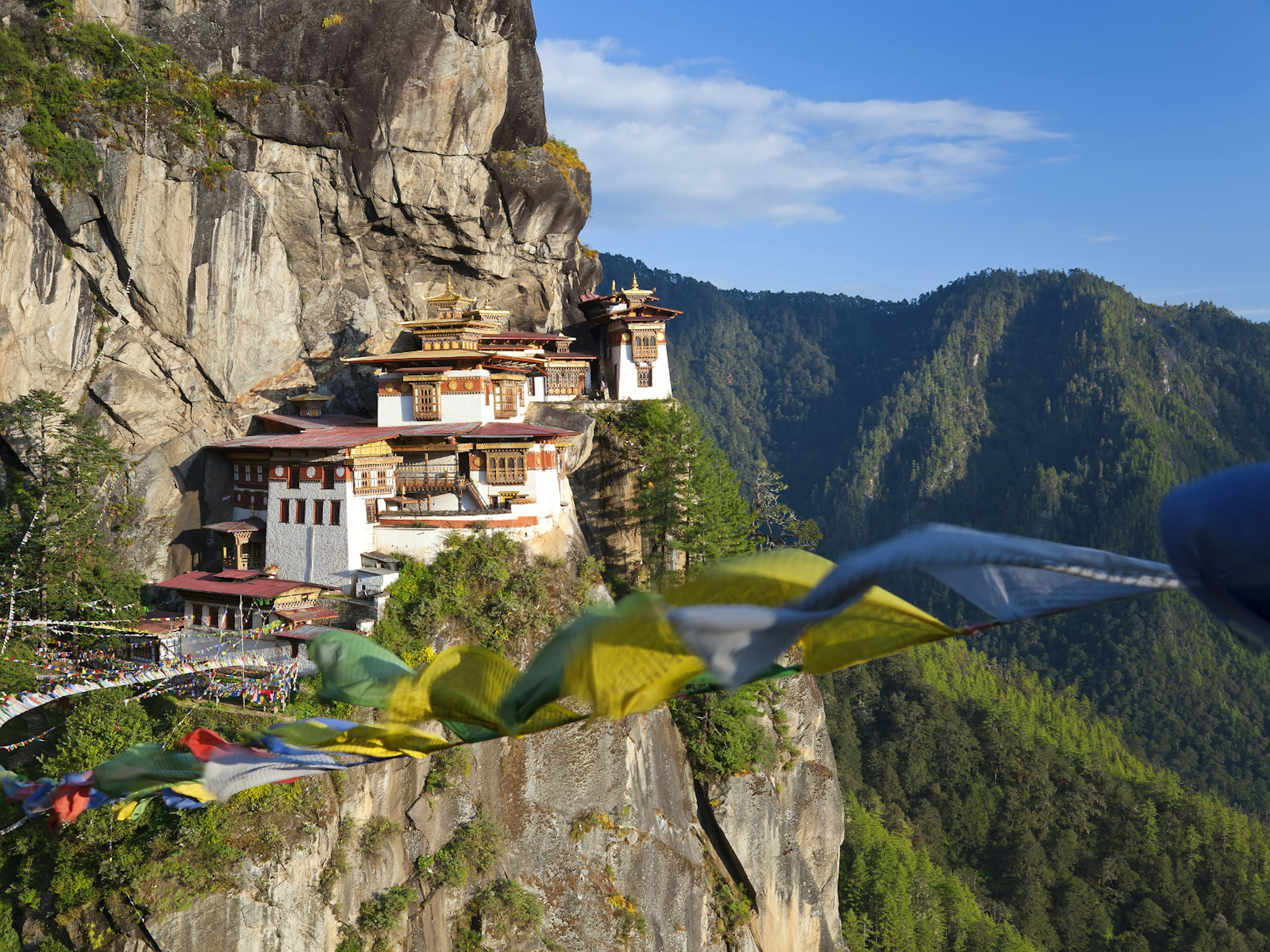 Tiger's Nest temple in Bhutan appears to be built in to the rock face of a mountain. Several colourful prayer flags are waving in the foreground