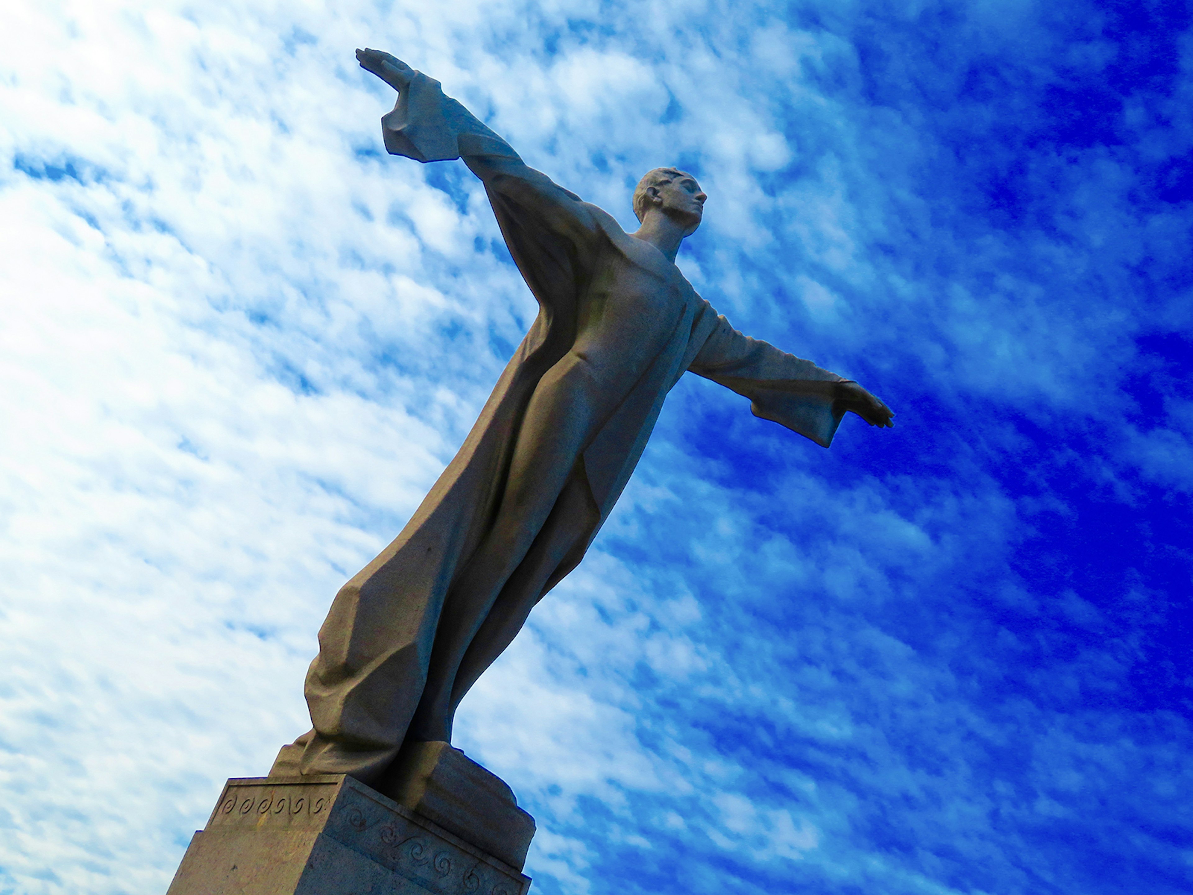 granite statue with outstretched arms against a blue sky in washington dc