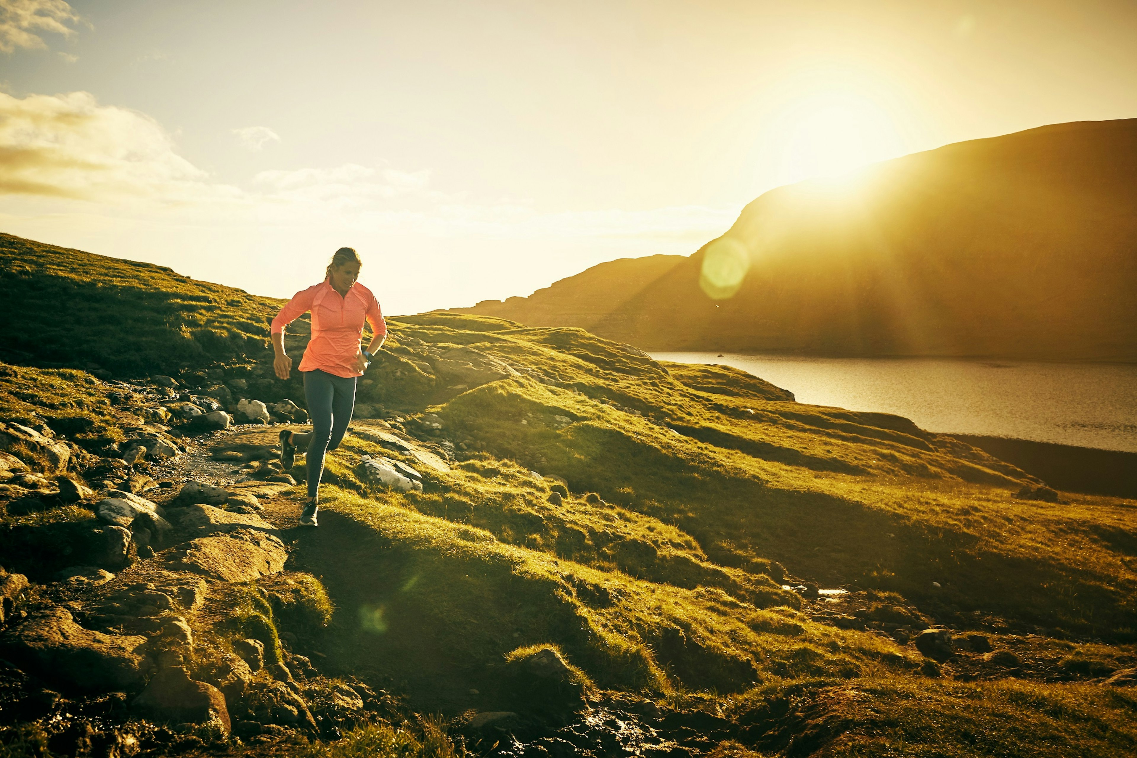 A woman runs along a section of rocky coast in Australia with the sun setting behind her.