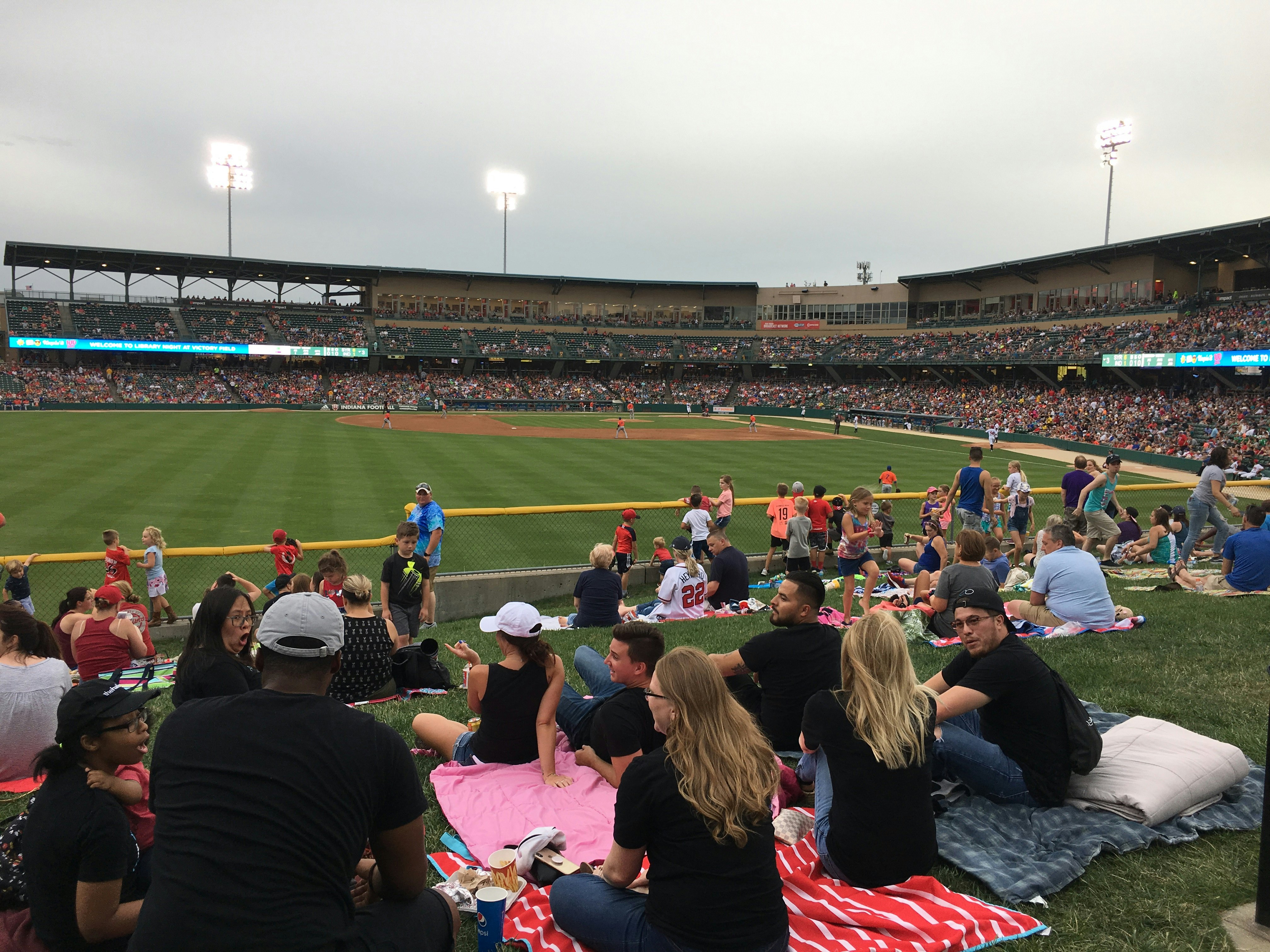 A group of people sit on blankets on a hill at a baseball field in Indianapolis