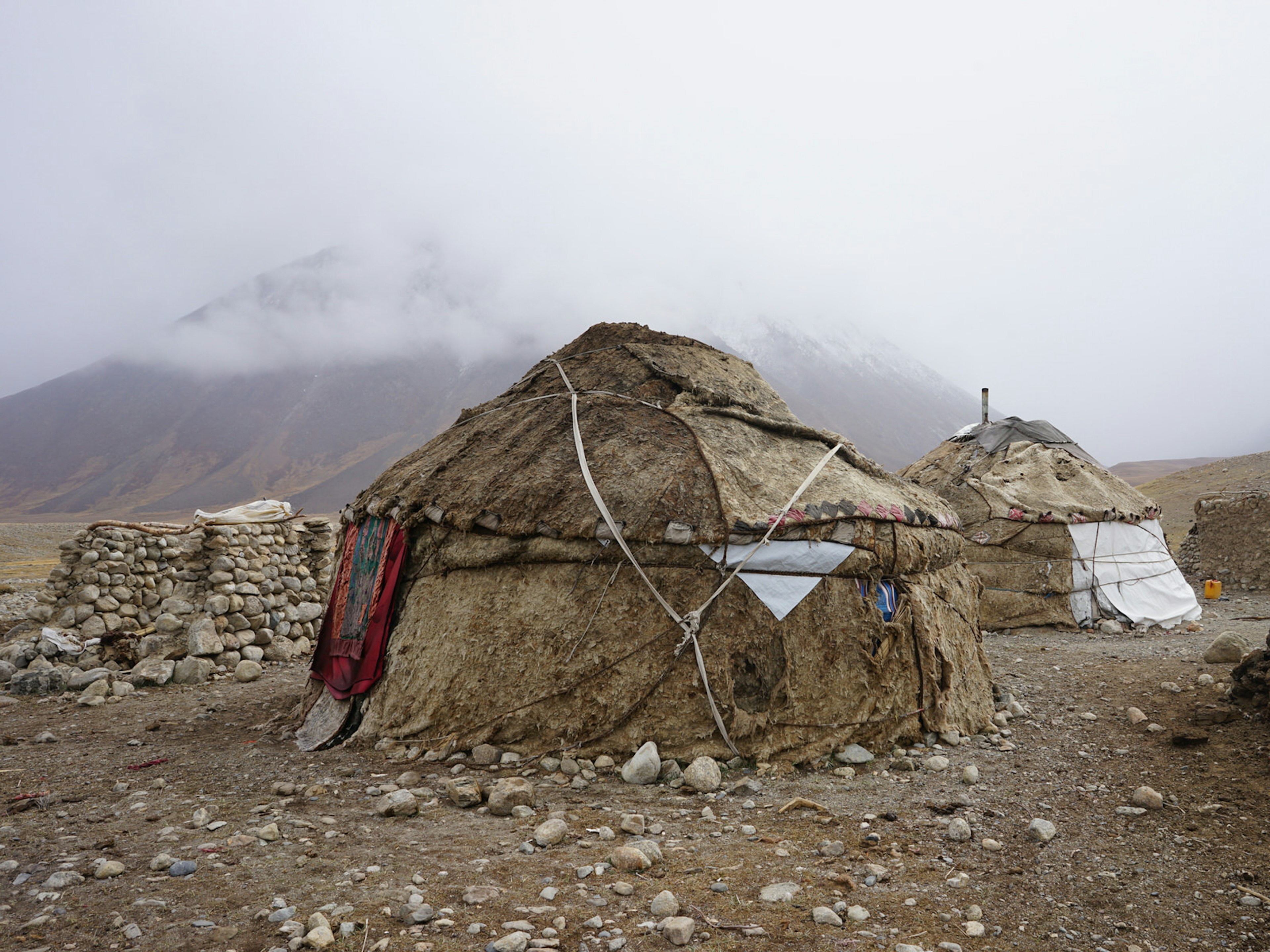 A traditional yurt tent camp made of wool and leather with mountains and fog in the background