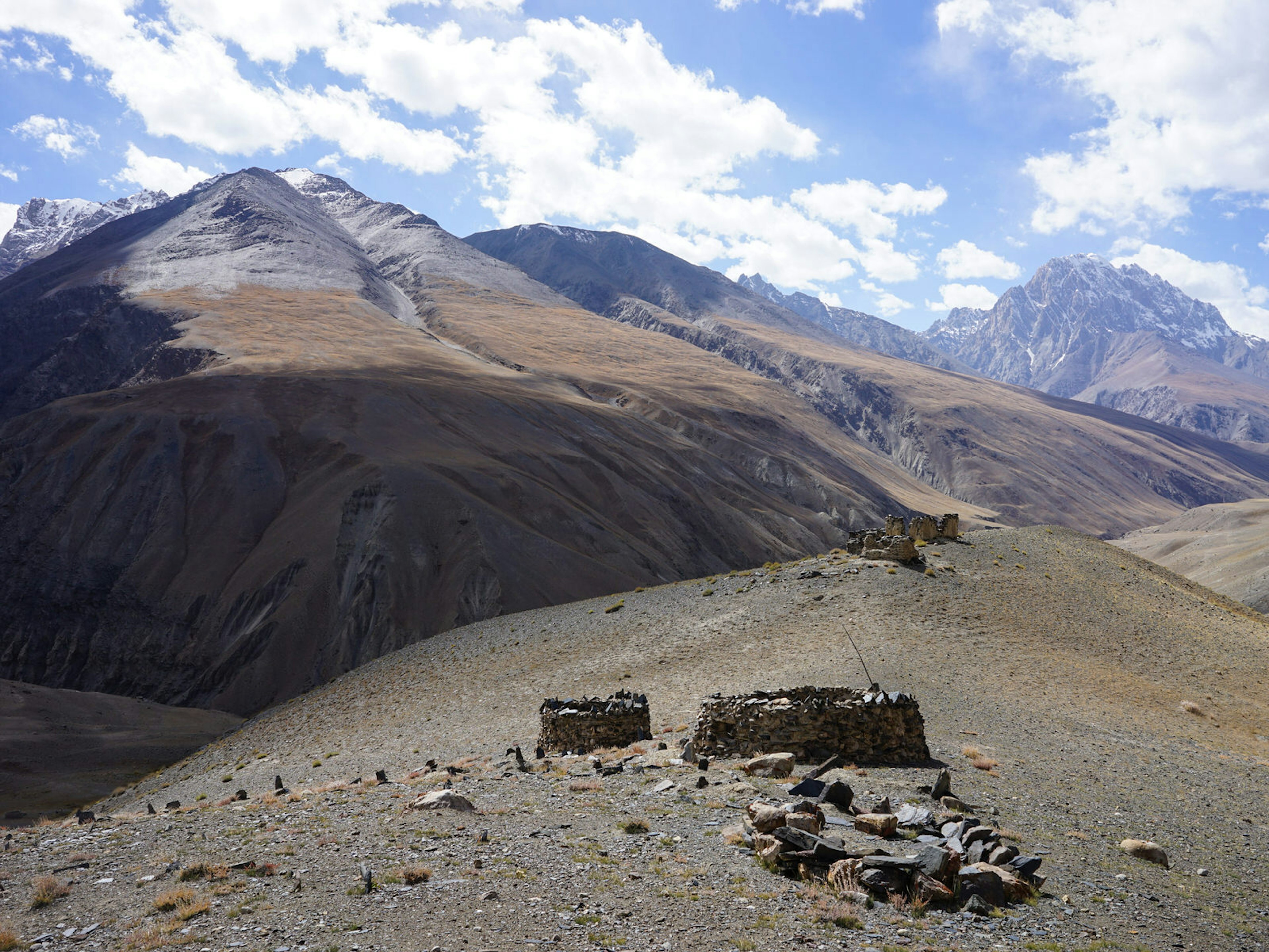 A small stone ruin sits atop a ridge in the foreground with tall mountains in the background