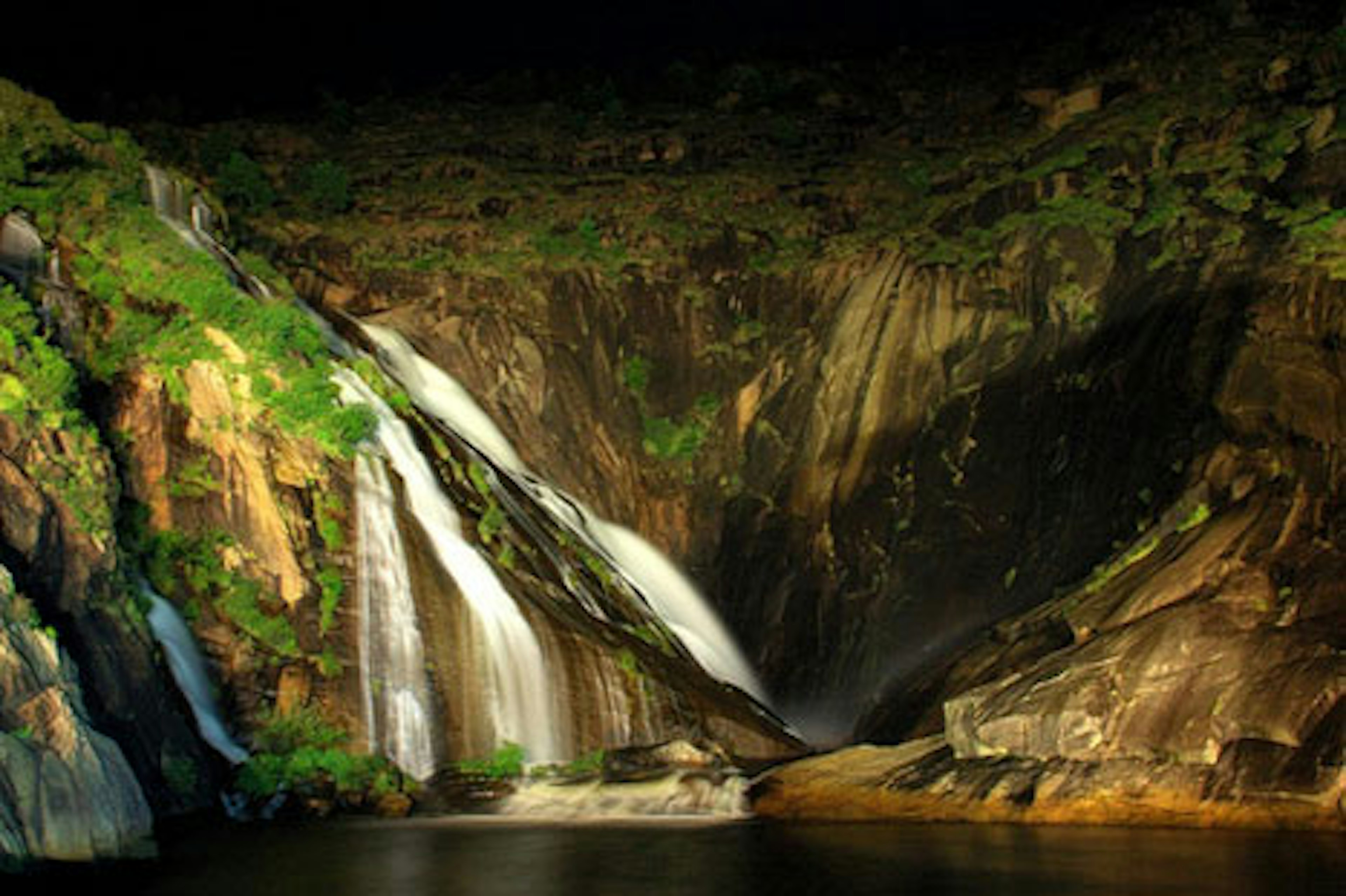 A glimmering waterfall runs over rocks into the sea