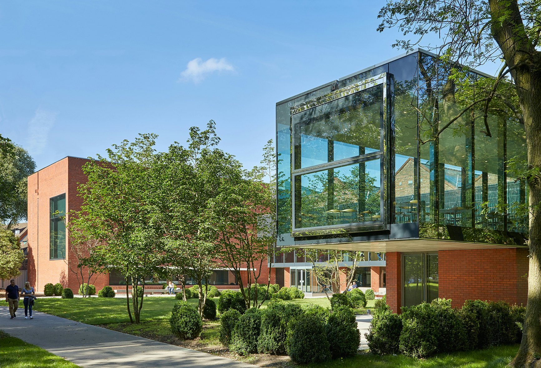 The Whitworth Art Gallery, Manchester; two people walk along a path in landscaped gardens towards the red-brick-and-glass building housing the gallery's cafe.