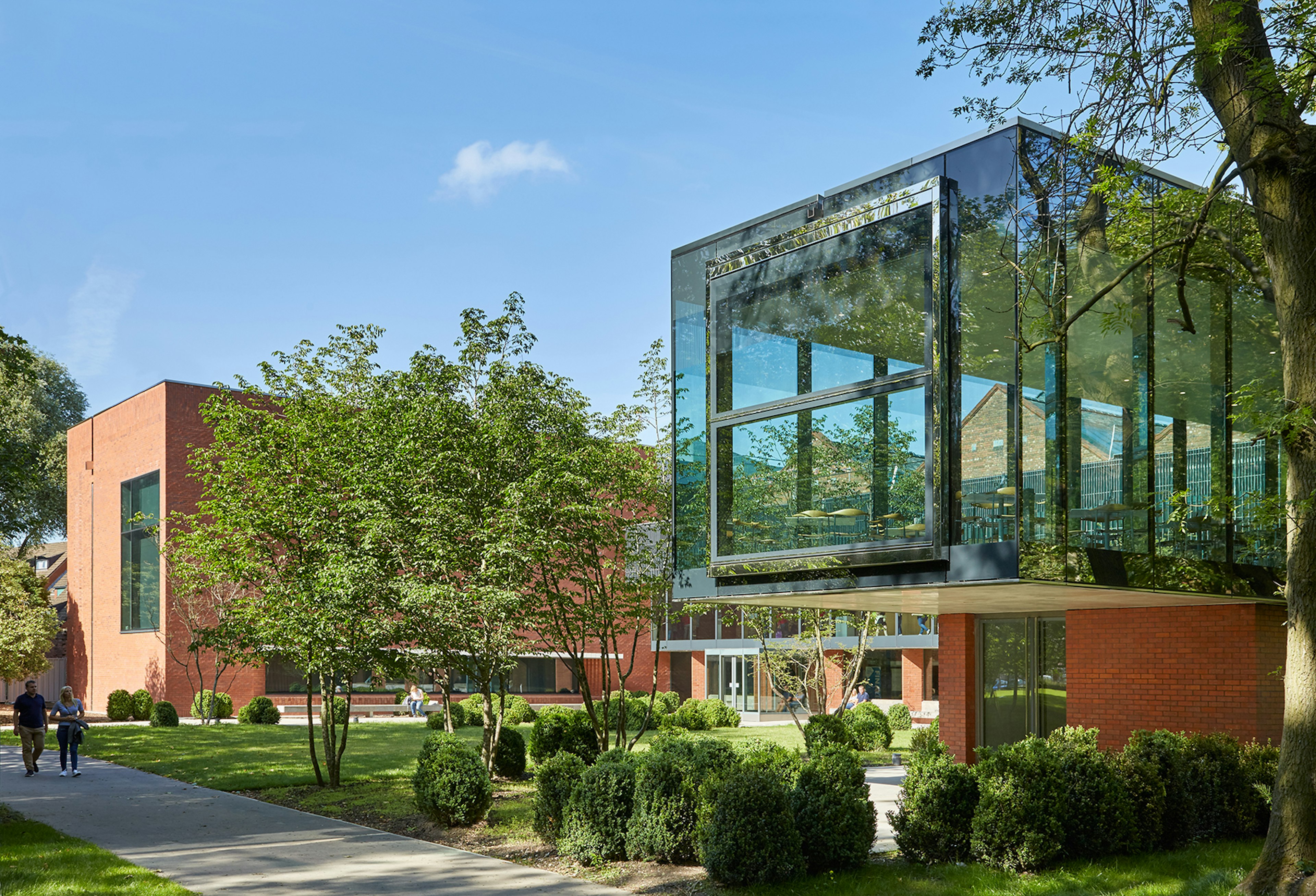 The Whitworth Art Gallery, Manchester; two people walk along a path in landscaped gardens towards the red-brick-and-glass building housing the gallery's cafe.