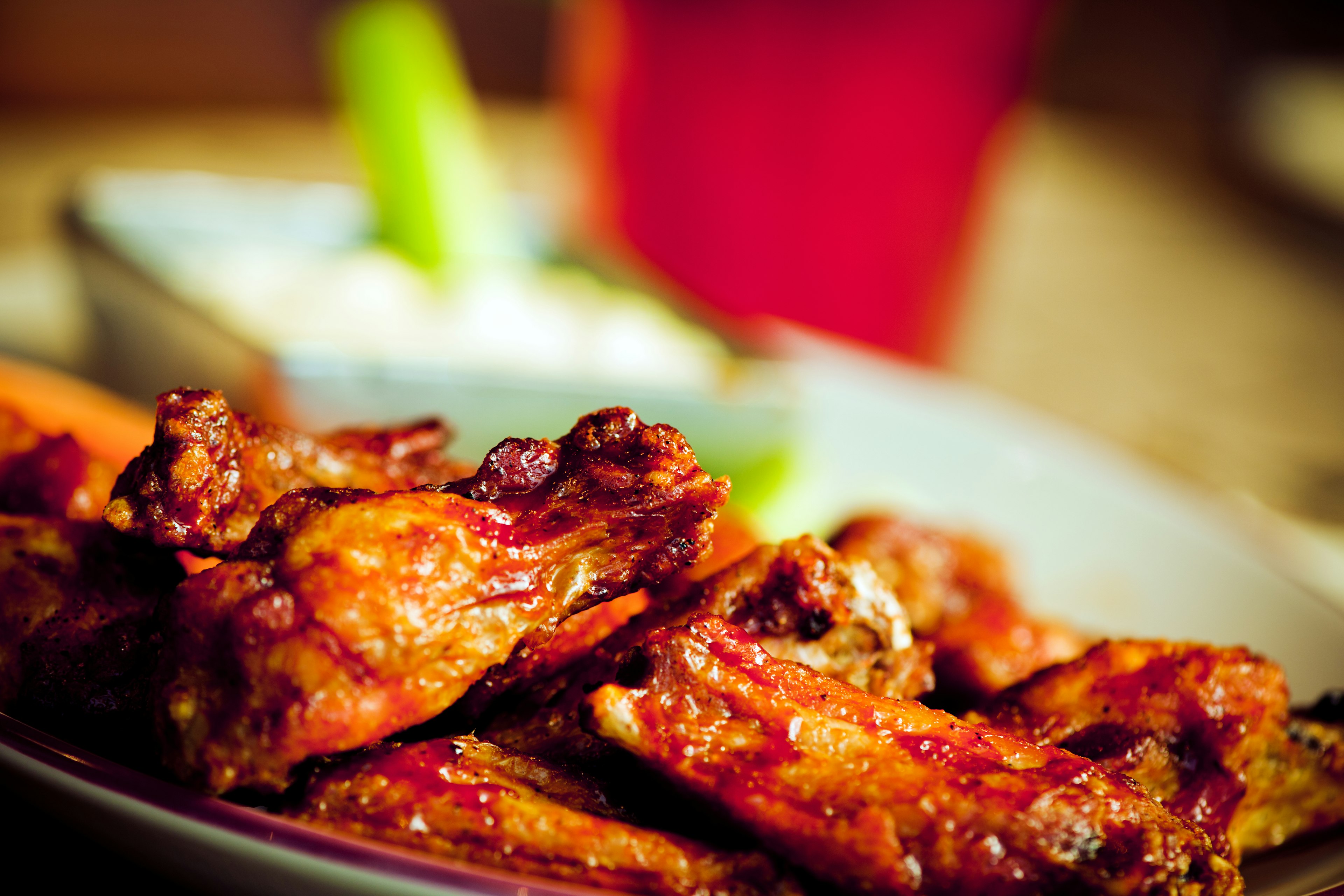 Closeup of a plate of buffalo wings. In the background you can see a dish of blue cheese and a drink; NFL bars