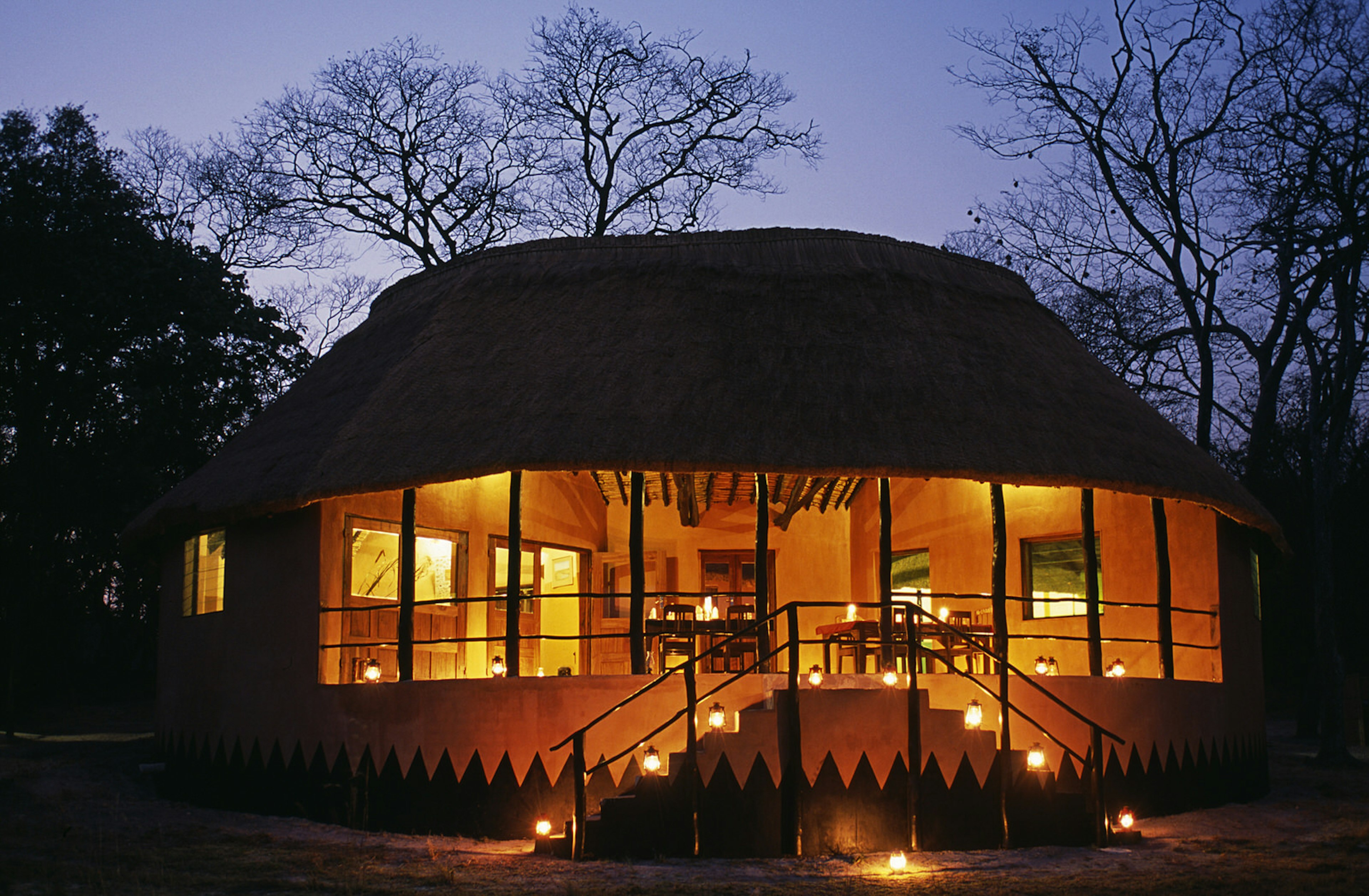 Taken at night, a warm glow - fuelled by gas lamps - lights up the interior of a thatch-roofed dining area.